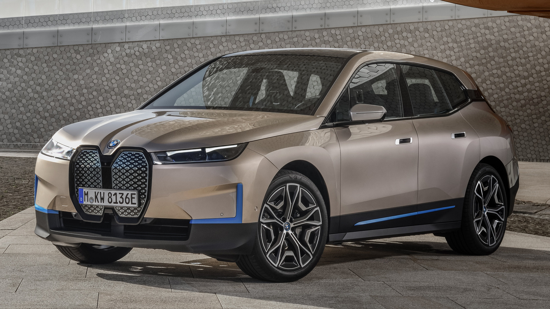 A 2022 BMW iX electric SUV parked in front of a modern textured wall. The iX showcases its distinctive futuristic design and two-tone color scheme