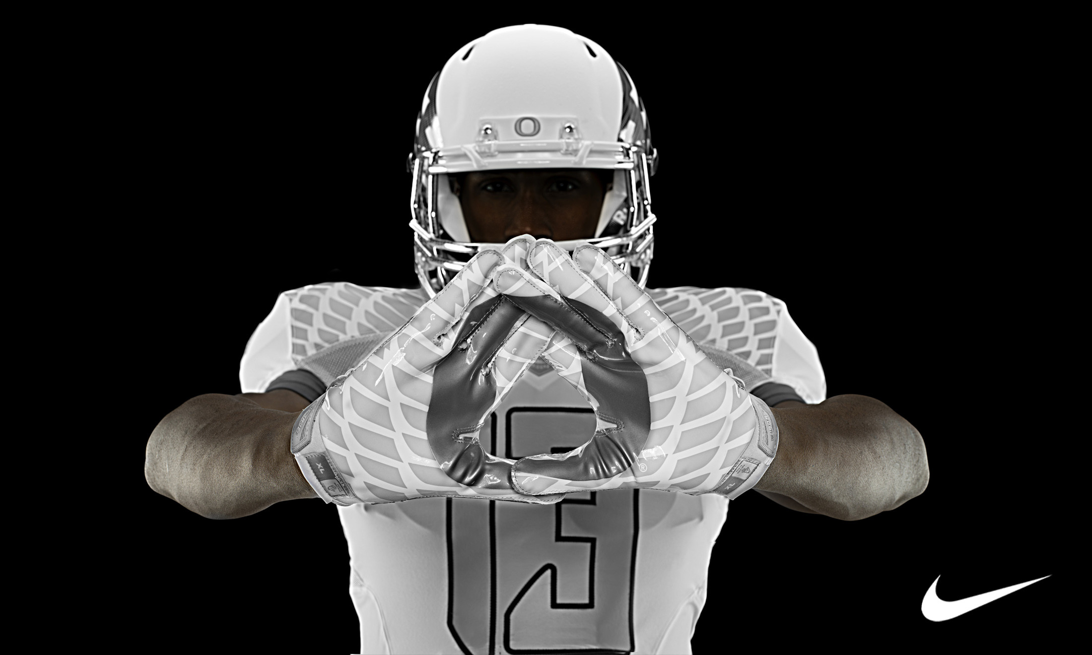 A football player in a Nike uniform and helmet, making a hand gesture against a black background
