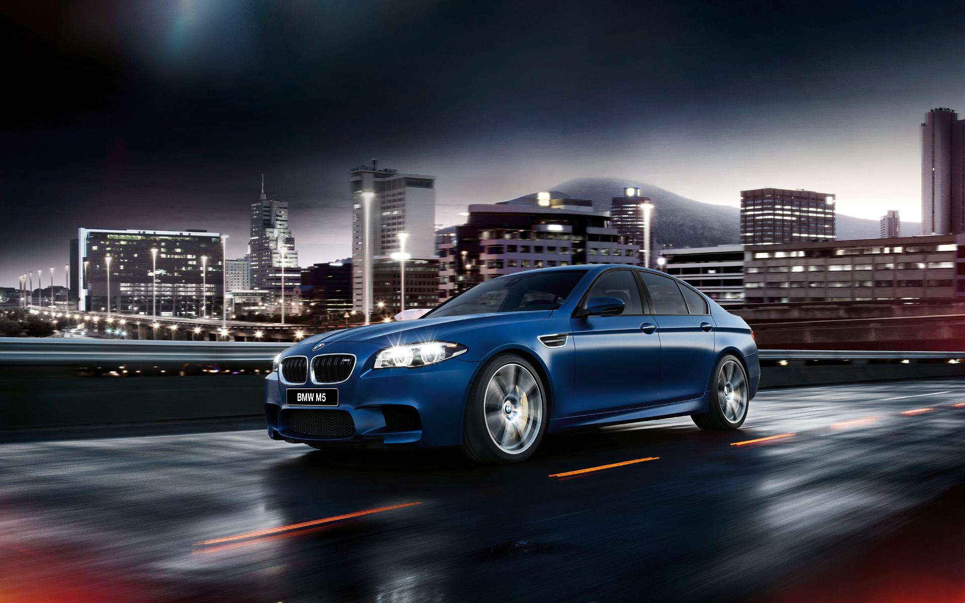 A sleek, blue BMW M5 speeding through a city at night