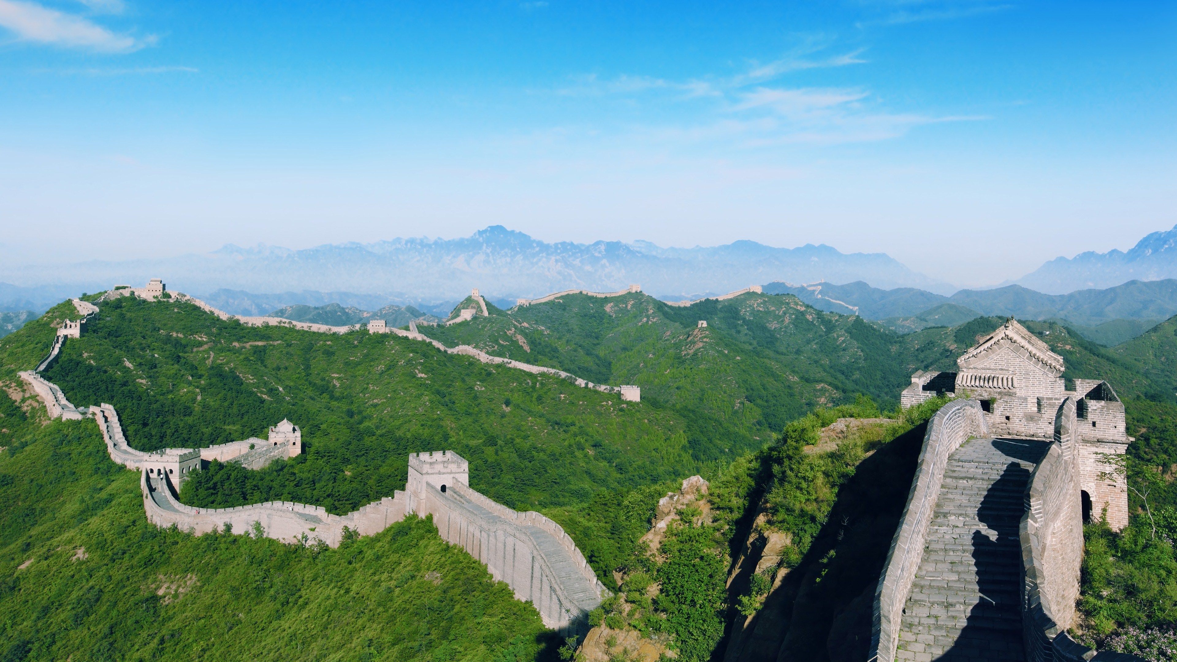 A panoramic view of the Great Wall of China snaking through lush green mountains under a vibrant blue sky