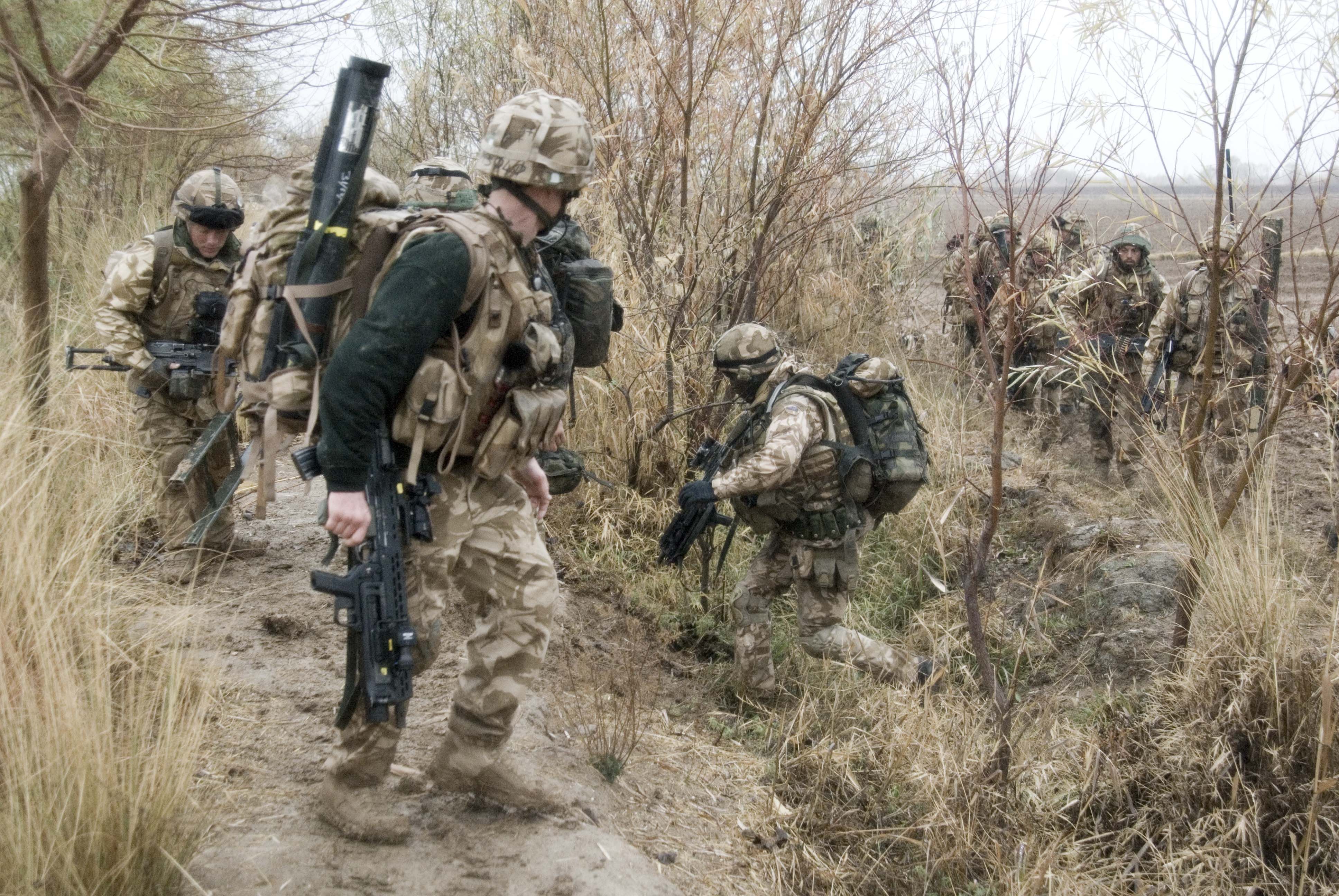 Soldiers in camouflage navigating a muddy path, possibly on patrol or during a military exercise