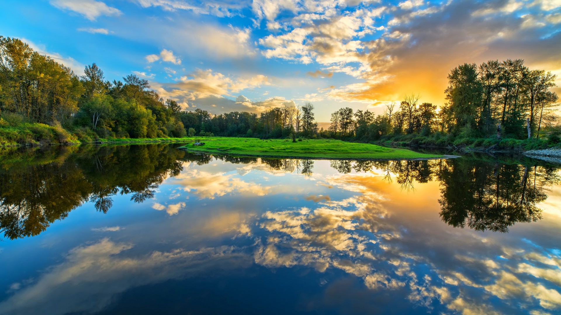 Stunning sunset reflected in calm river surrounded by lush trees and grass