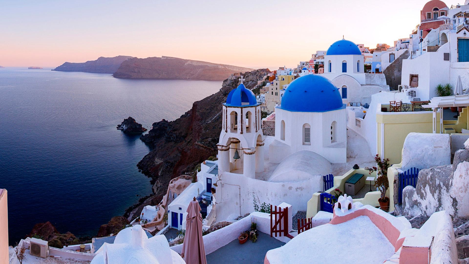 White-washed buildings with blue domes overlooking the Aegean Sea in Santorini, Greece at sunset