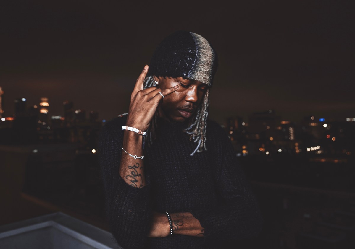 Ken Carson posing thoughtfully against a nighttime cityscape backdrop
