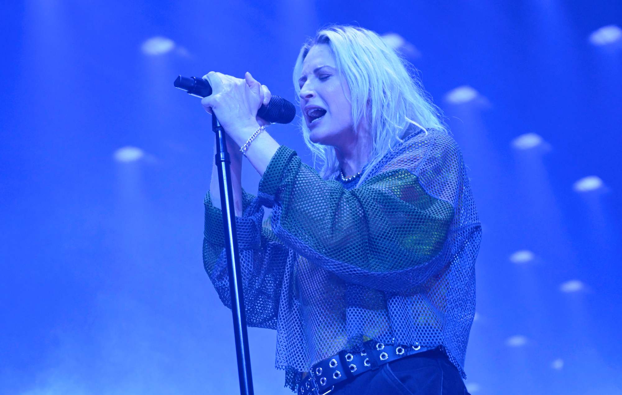 Emily Armstrong singing into a microphone on stage, illuminated by blue light