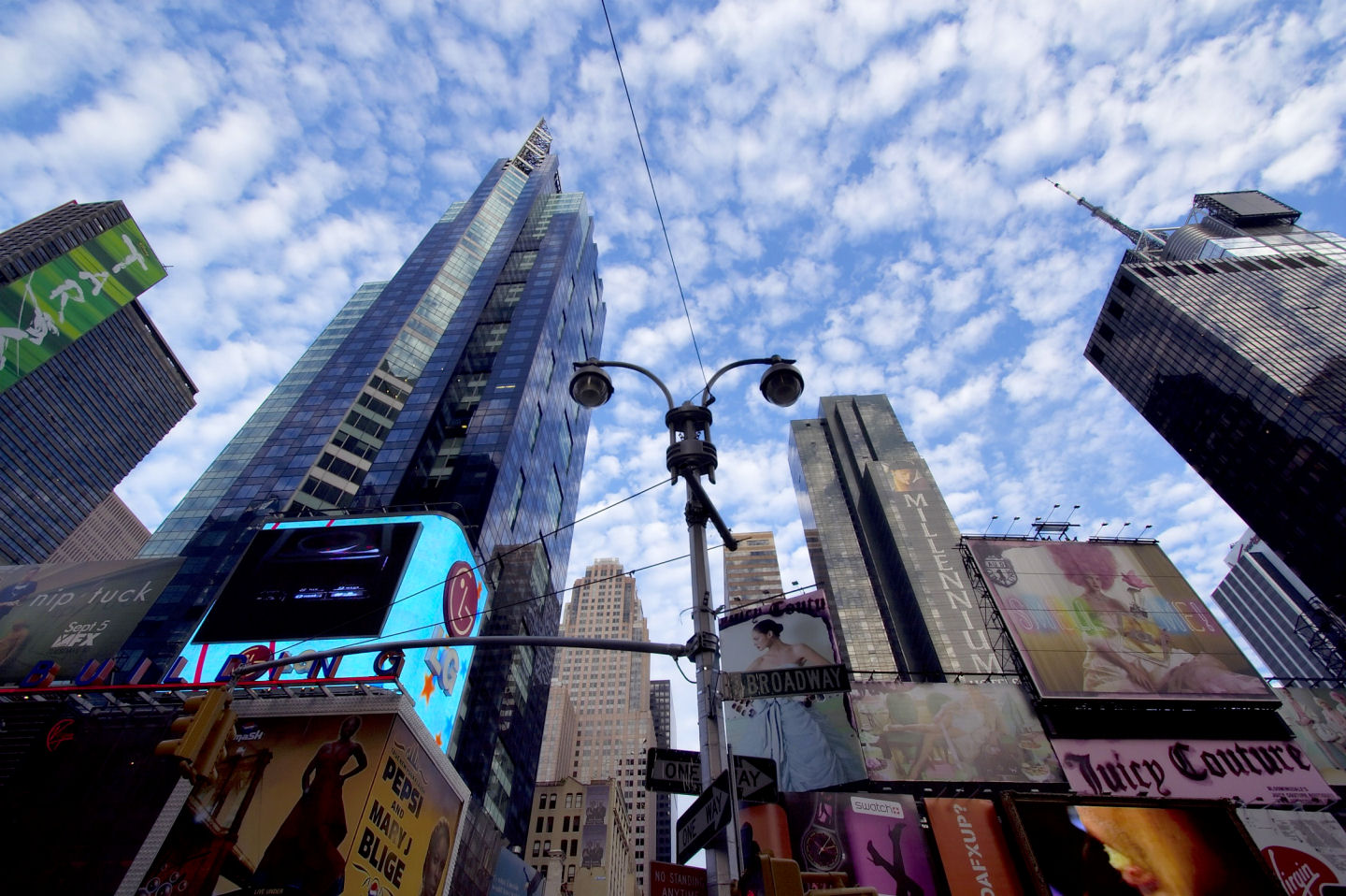 Low-angle view of Times Square, New York City, featuring vibrant billboards, towering skyscrapers, and a cloudy sky