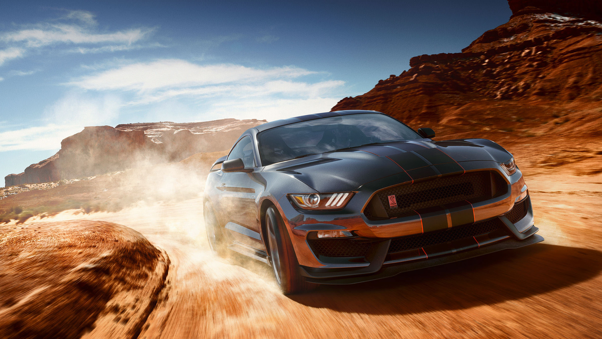 A dark gray Ford Mustang Shelby GT350 races through a desert landscape, kicking up a cloud of dust