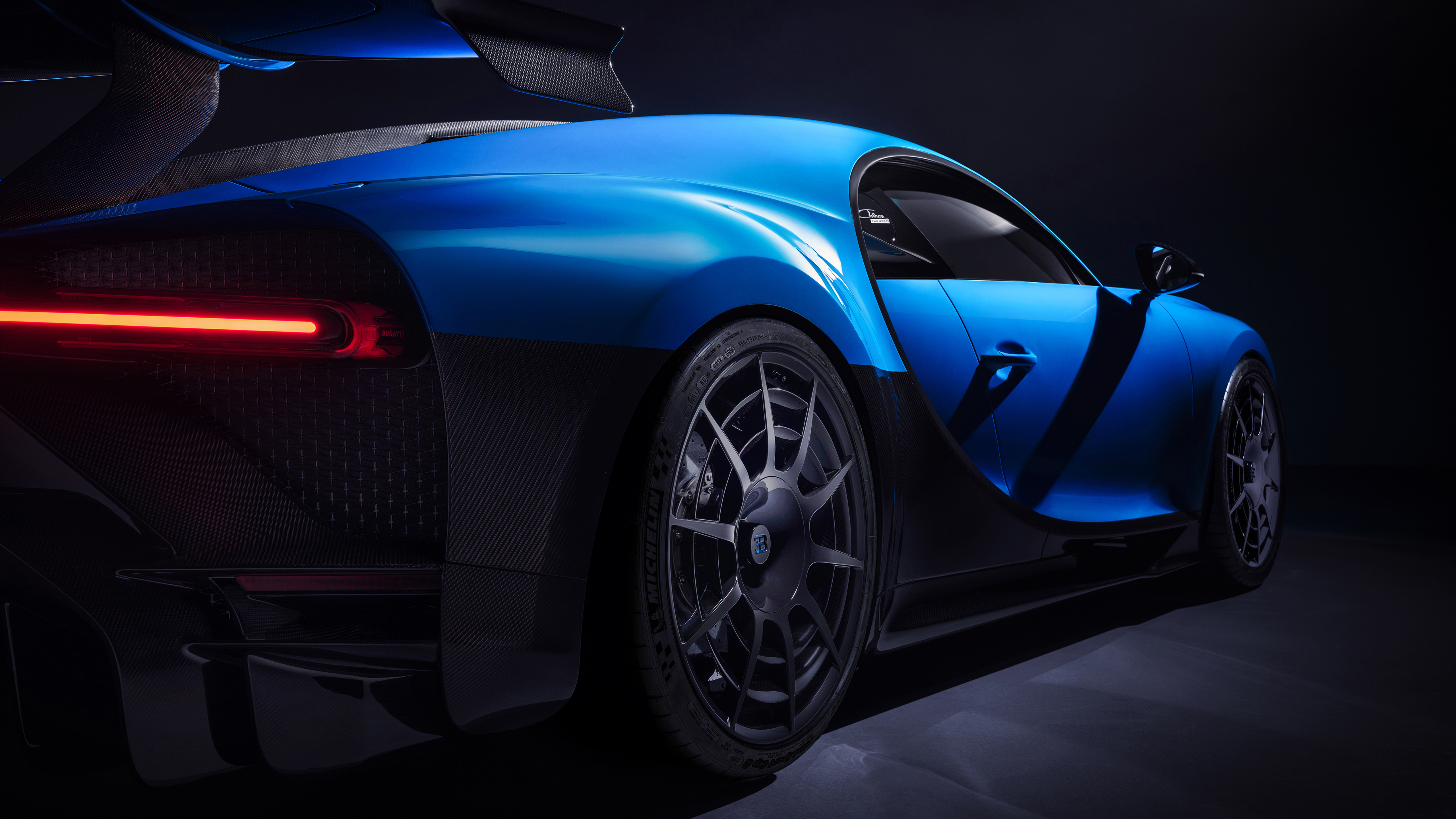 Close-up rear view of a sleek, blue Bugatti sports car with intricate wheel design and carbon fiber accents, highlighting its speed and luxury