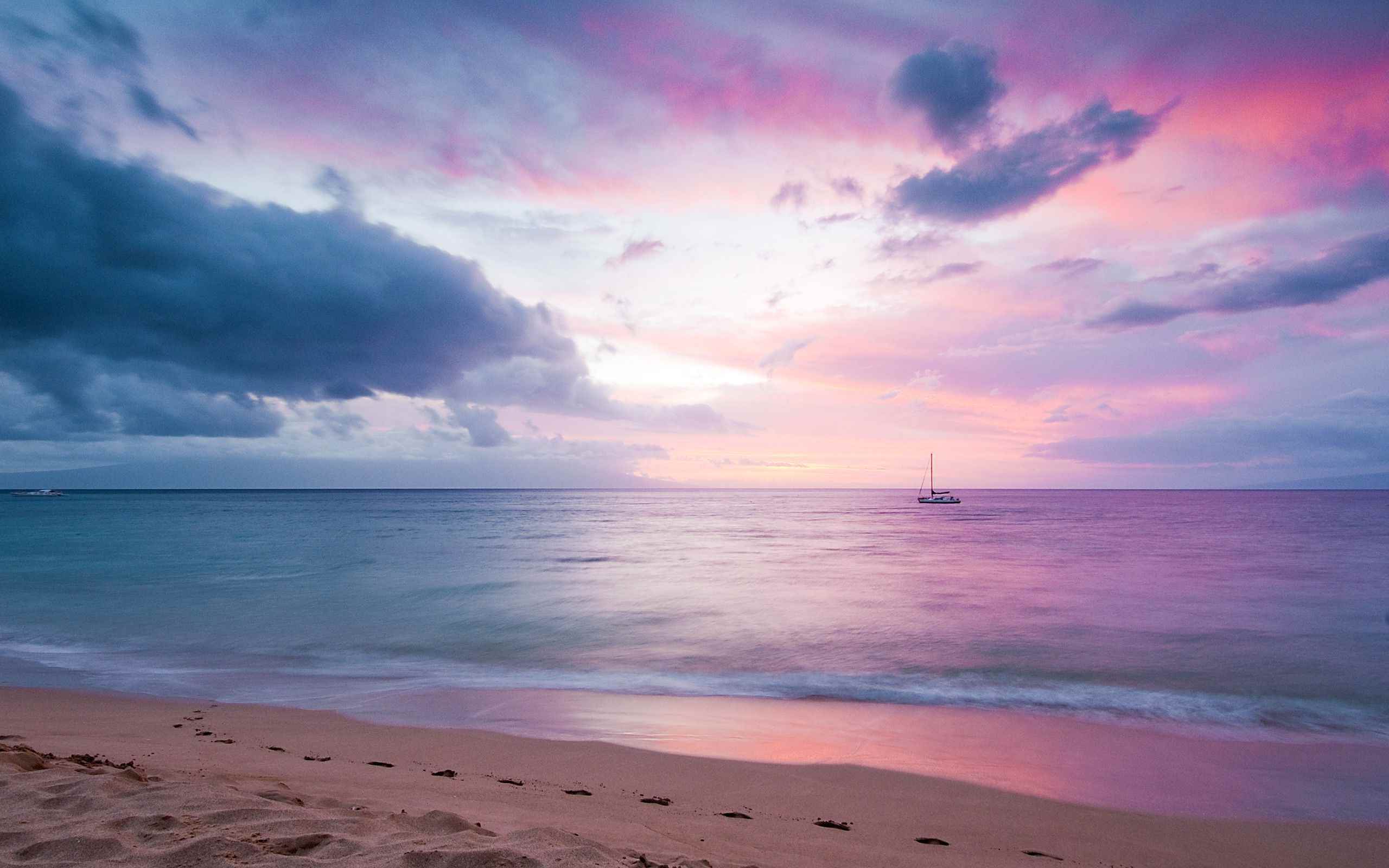 A serene beach at sunset with a sailboat in the distance, perfect for a calming computer background
