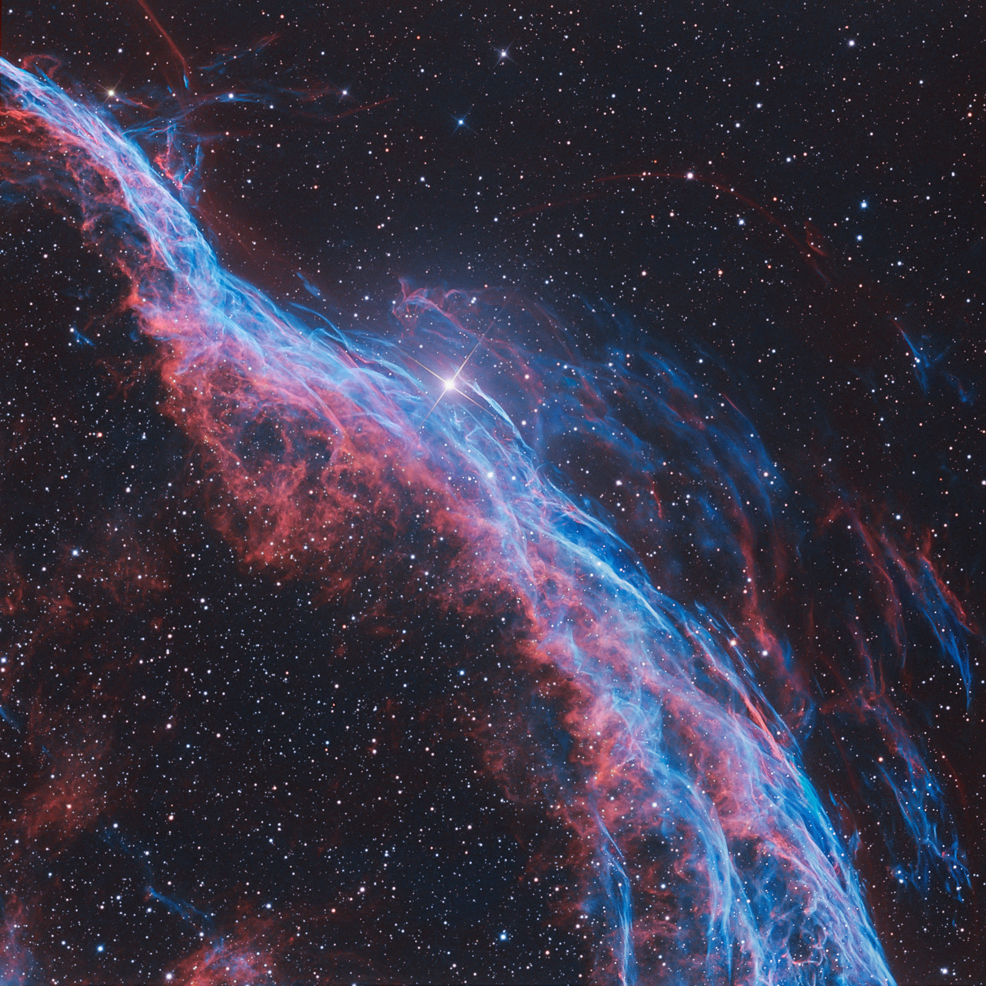 A breathtaking view of the Veil Nebula, showcasing its delicate filaments of red and blue gas against a backdrop of distant stars