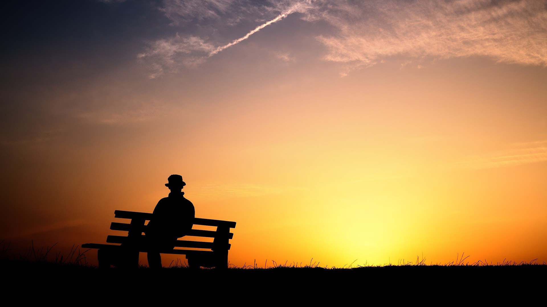 Silhouette of a lone person sitting on a bench at sunset, evoking a sense of contemplation and melancholy
