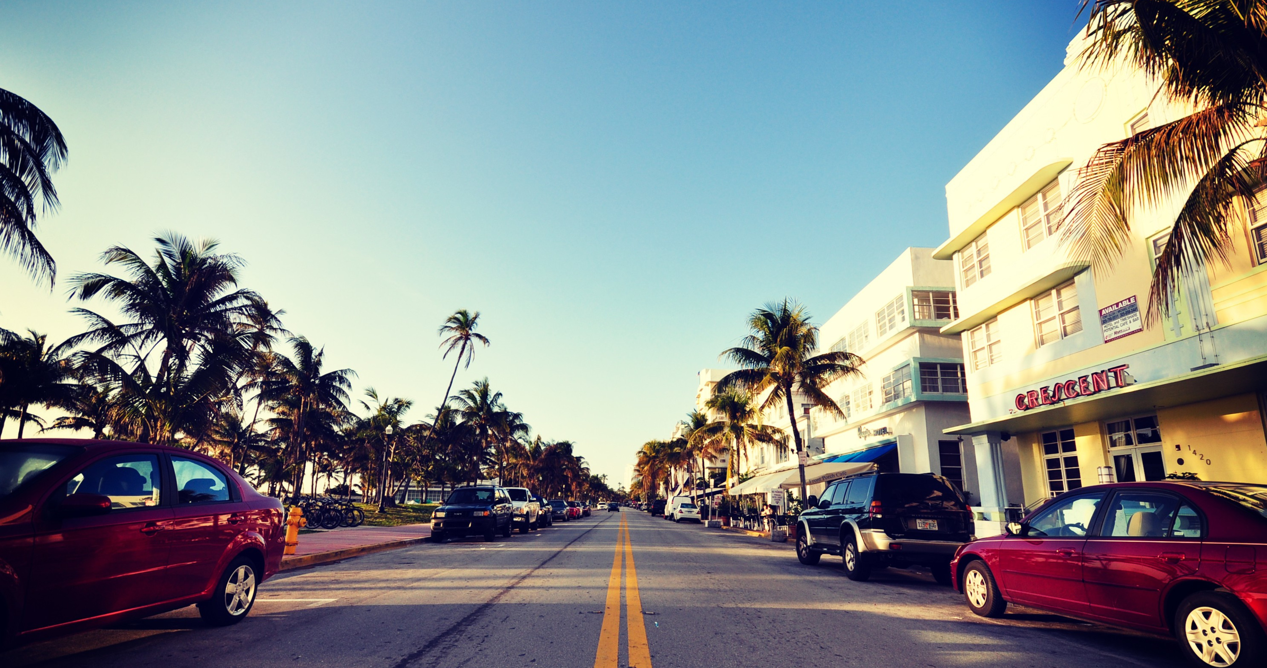 Vintage-style photo of Ocean Drive in Miami Beach, Florida, featuring Art Deco hotels, palm trees, and parked cars
