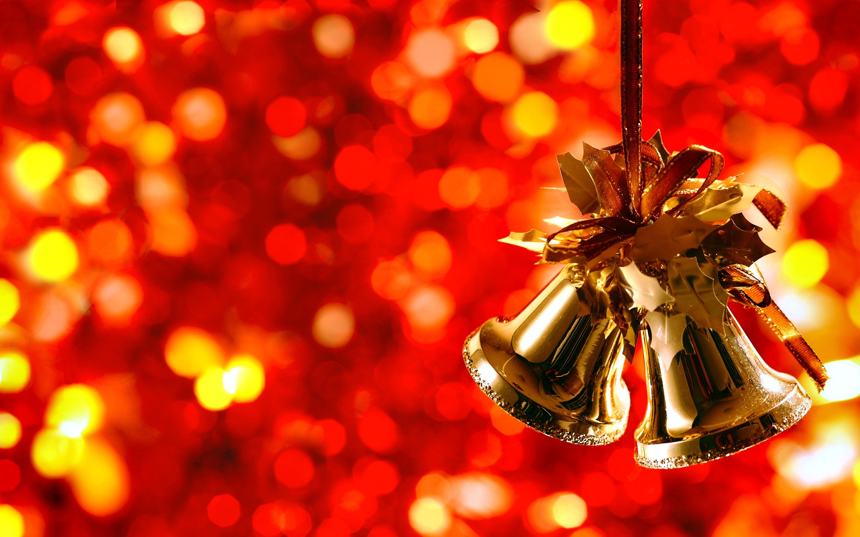 Golden Christmas bells hanging against a blurred background of red and gold Christmas lights, evoking a festive holiday spirit
