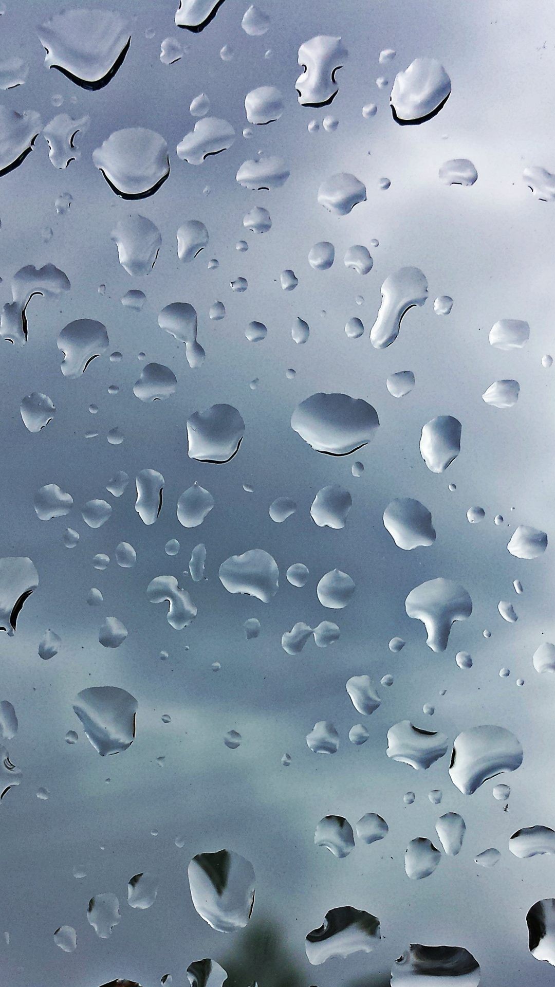 Close-up of raindrops clinging to a window pane against a blurred gray sky