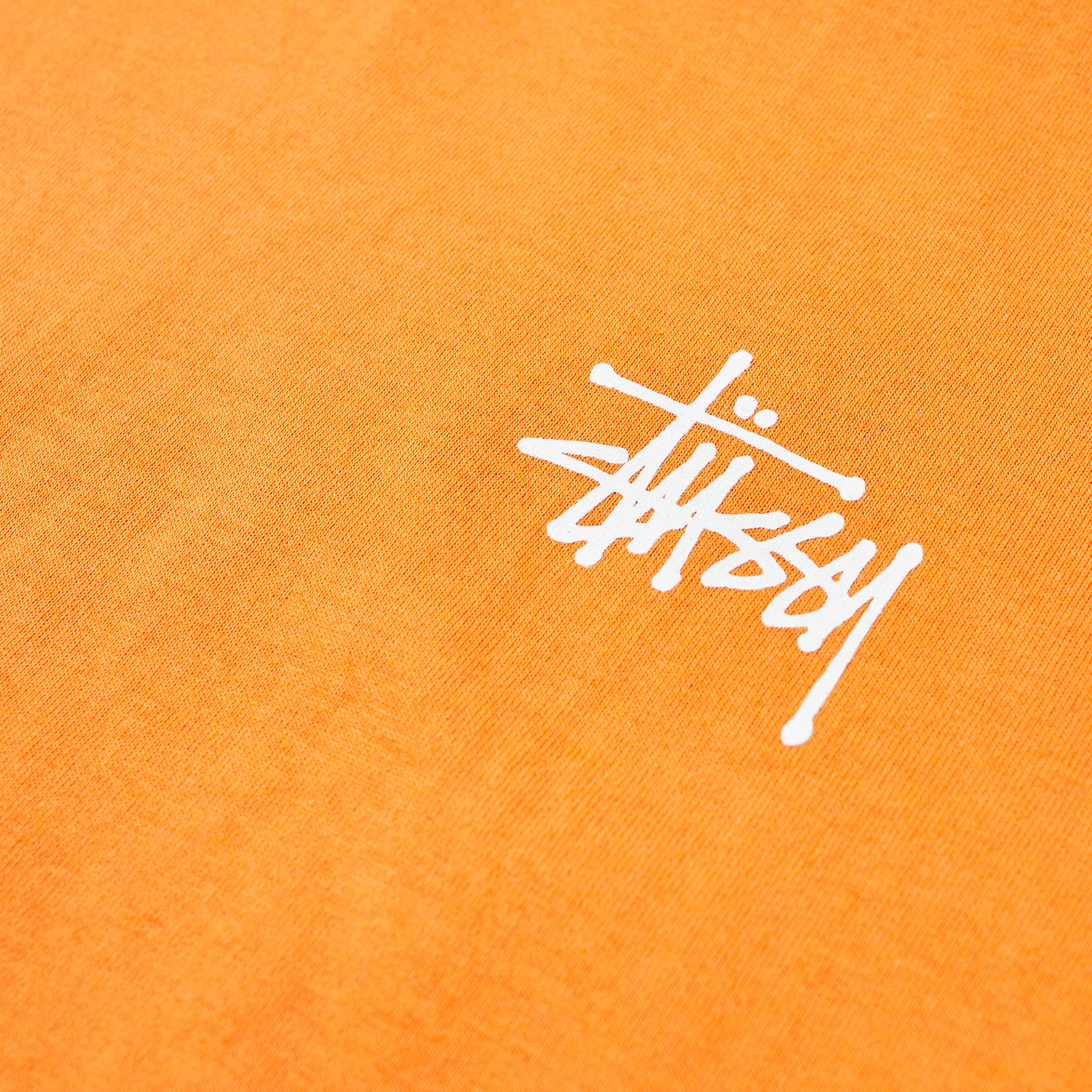 Close-up of a vibrant orange Stussy t-shirt featuring the iconic Stussy logo in white