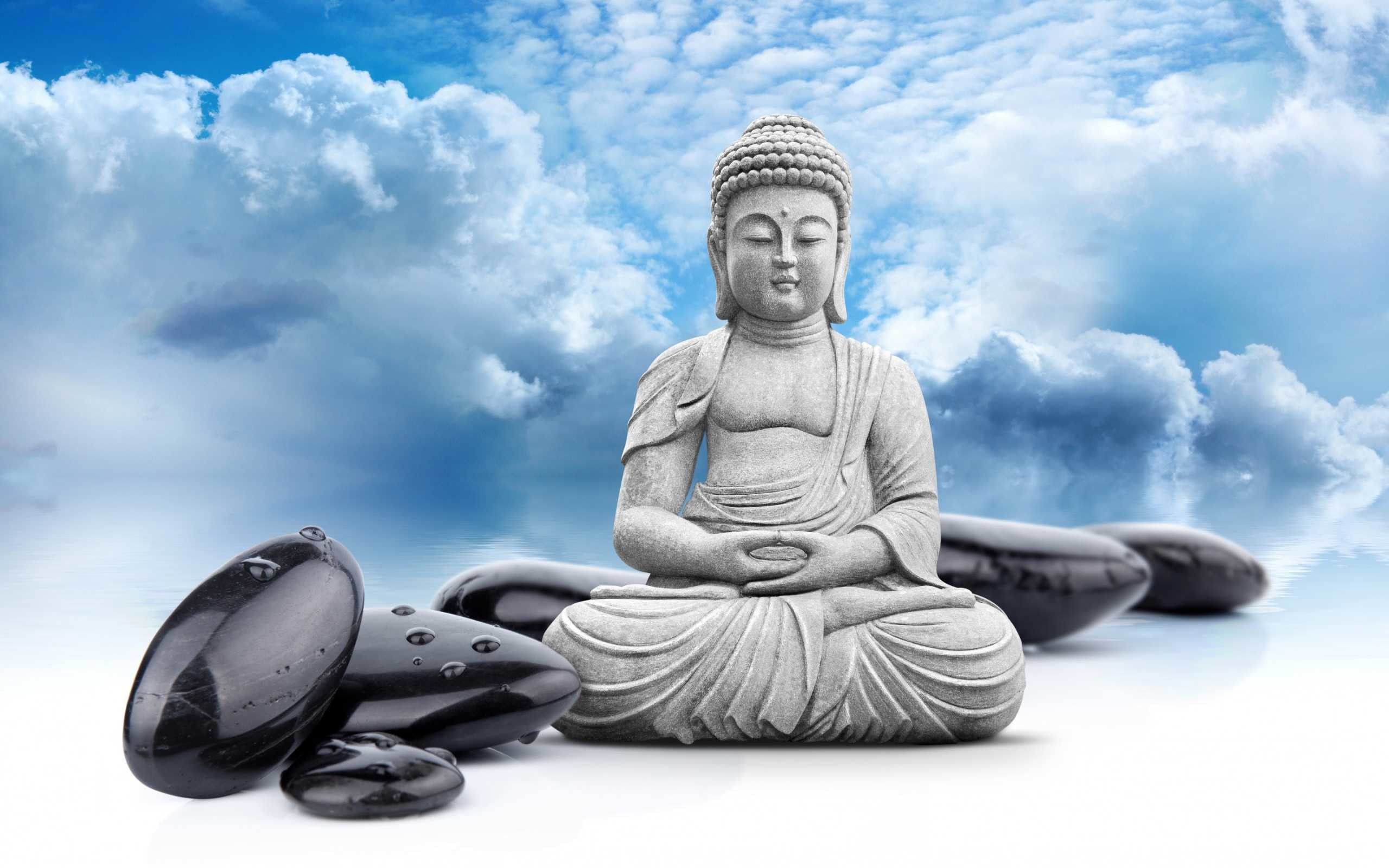 Serene Buddha statue meditating amidst black stones against a backdrop of tranquil blue sky and white clouds, evoking peace and mindfulness