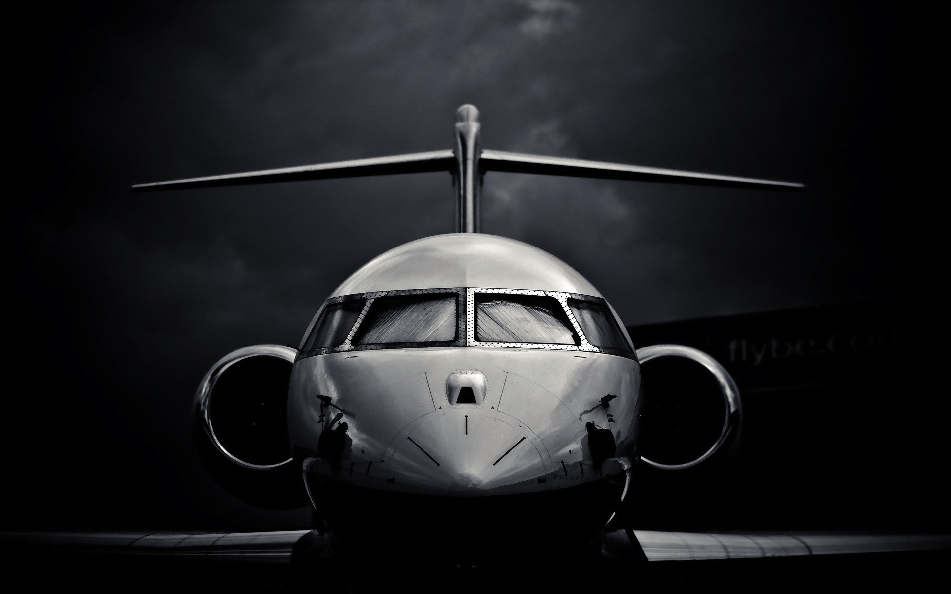 Dramatic black and white photo of a private jet's cockpit against a dark, cloudy sky