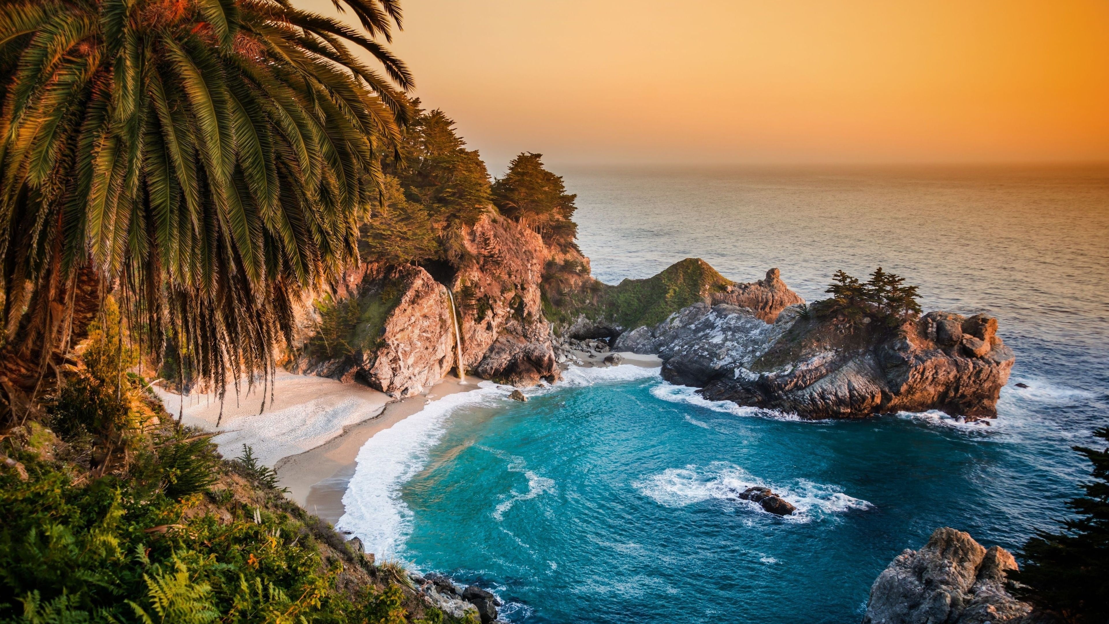 A breathtaking sunset illuminates the McWay Falls in Julia Pfeiffer Burns State Park, California, as it cascades onto a pristine beach nestled between rocky cliffs and turquoise waters
