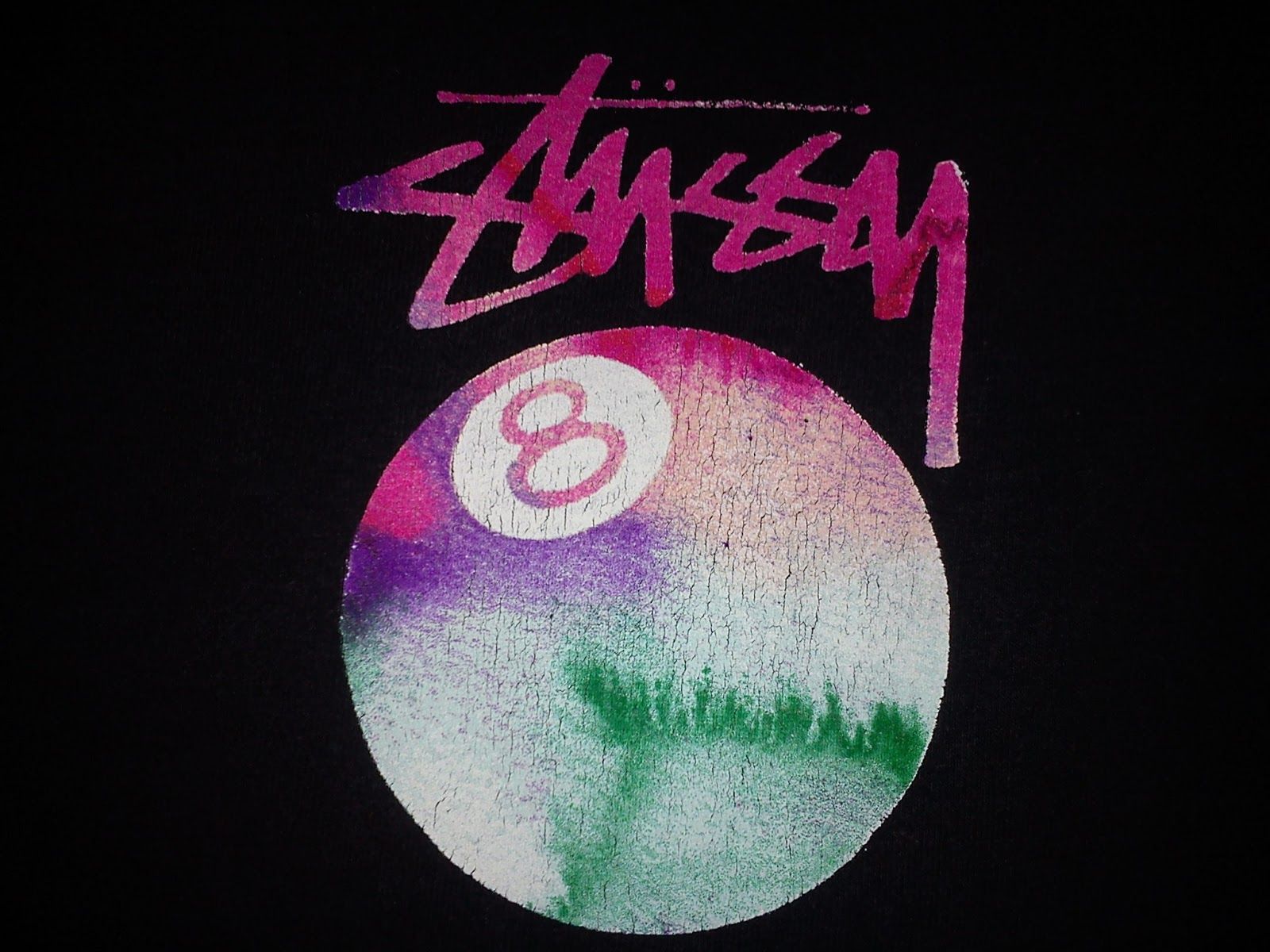 Close-up of a Stussy t-shirt featuring a colorful 8-ball design with a cracked texture and the signature Stussy logo