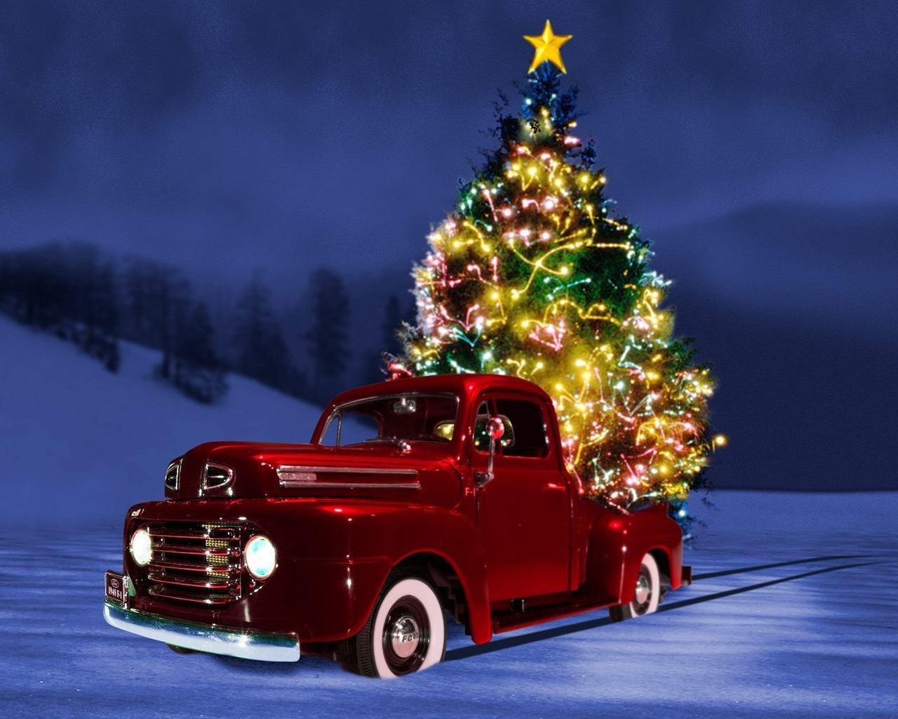 A vintage red truck carrying a brightly lit Christmas tree through a snowy landscape