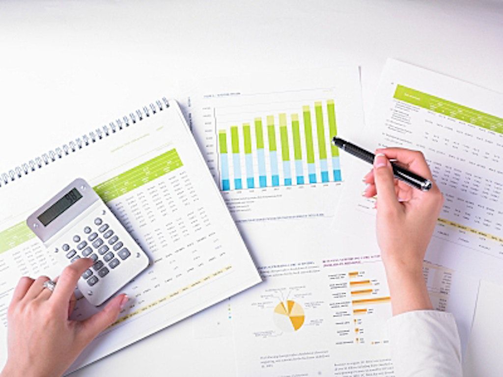 Hands working on accounting reports and charts, using a calculator and pen for analysis