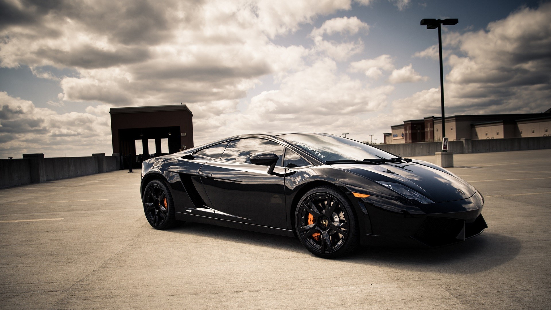 Sleek Black Lamborghini Gallardo parked on a rooftop parking lot under a cloudy sky