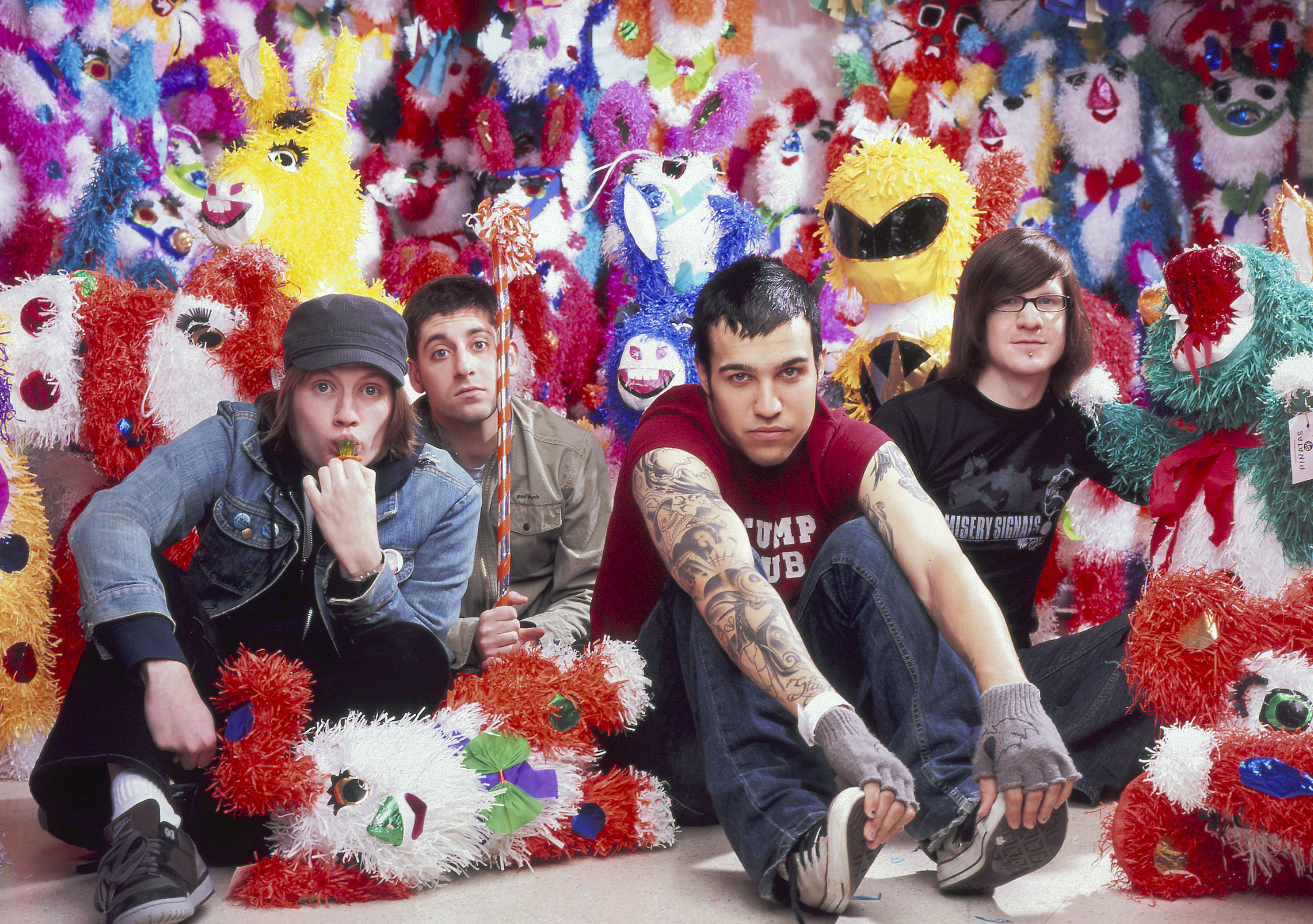 Fall Out Boy band members pose amidst a colorful backdrop of piñatas