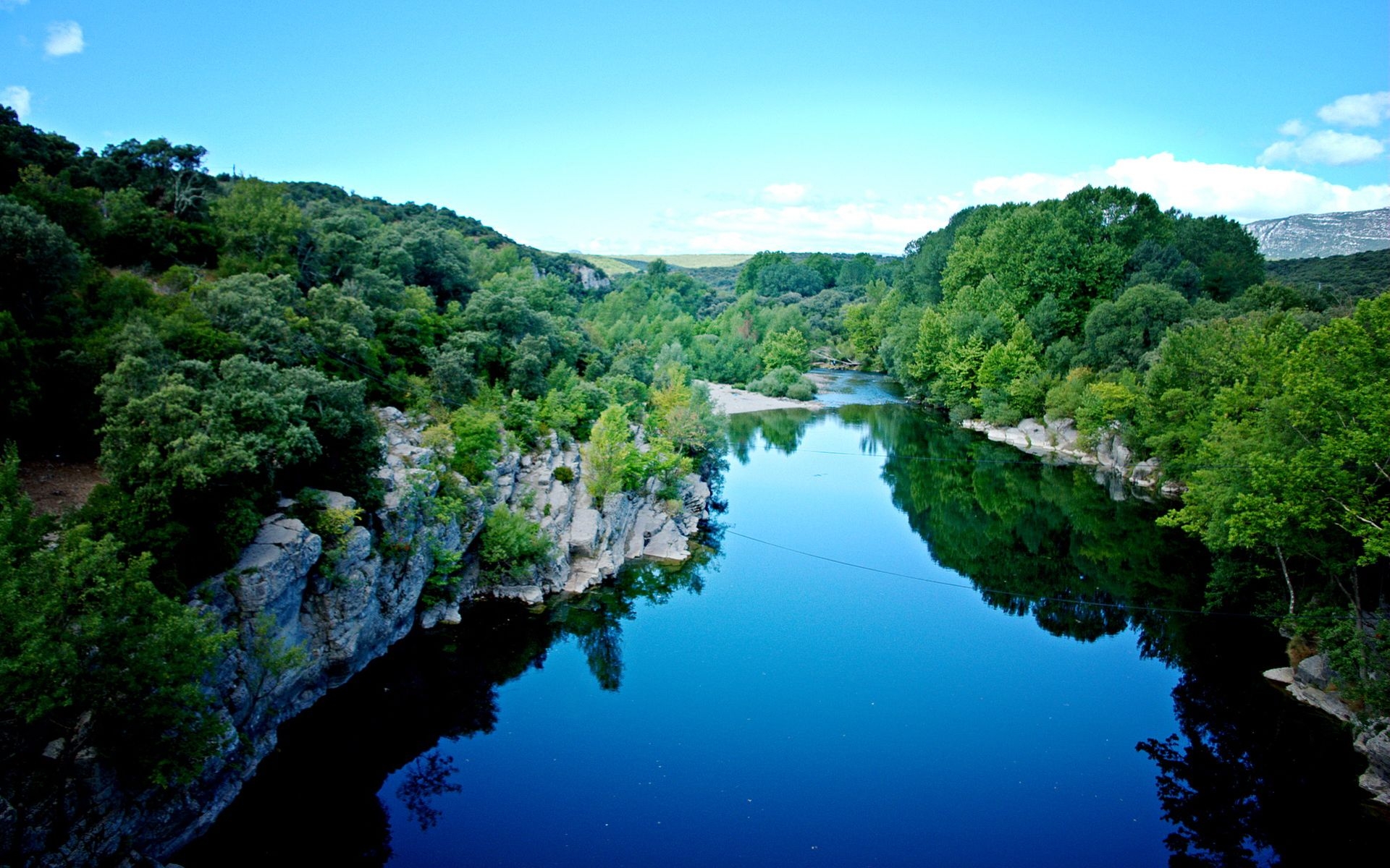 A breathtaking aerial view of a serene river flowing through a lush green valley, reflecting the clear blue sky. Perfect for a desktop wallpaper