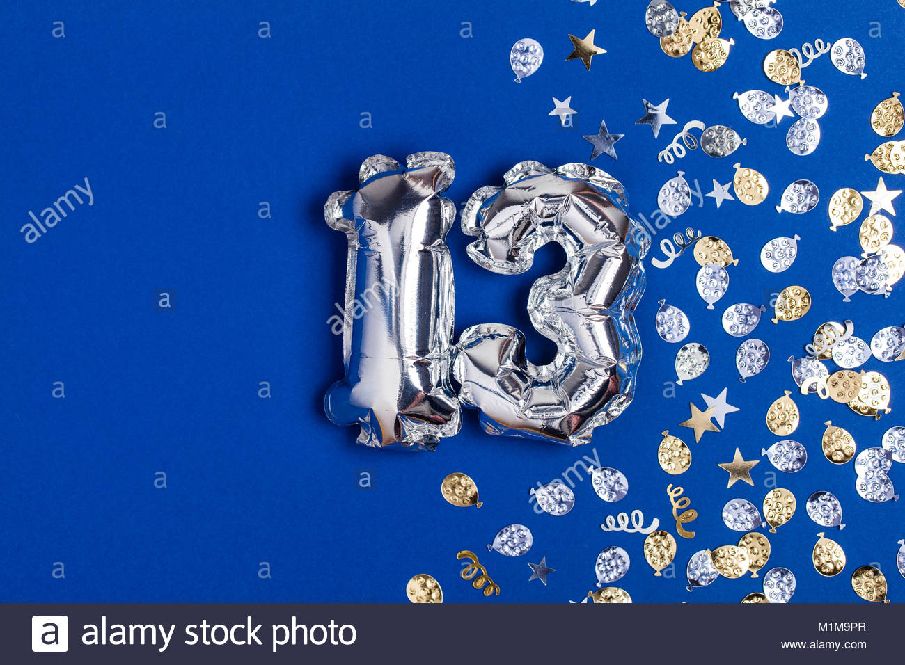 Silver foil number 13 balloon on a blue background with glitter