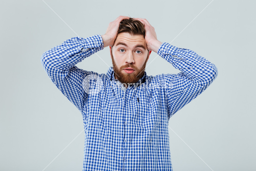 Worried Bearded Young Man Standing With Hands On Head Over White