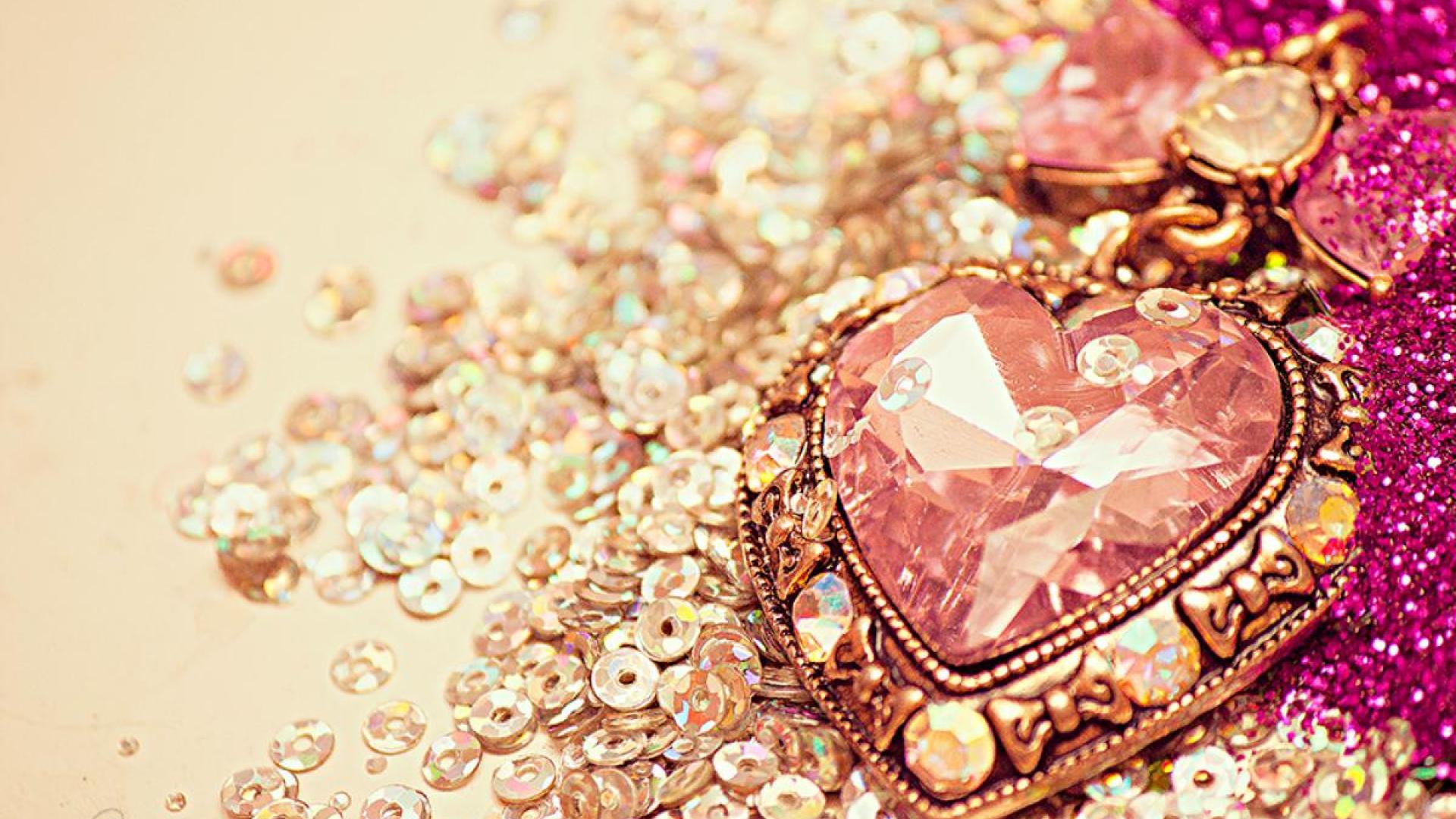 A close-up of a heart-shaped pendant adorned with pink gemstones, resting on a bed of sparkling sequins. This romantic image evokes feelings of love, luxury, and glamour