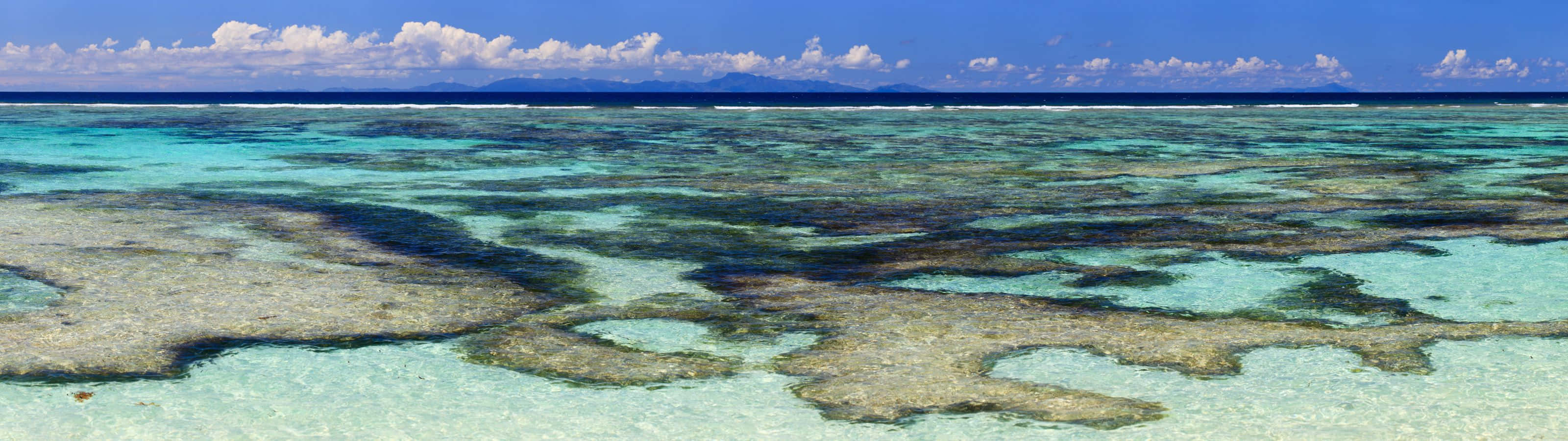 Shallow turquoise water over a coral reef, with islands in the distance