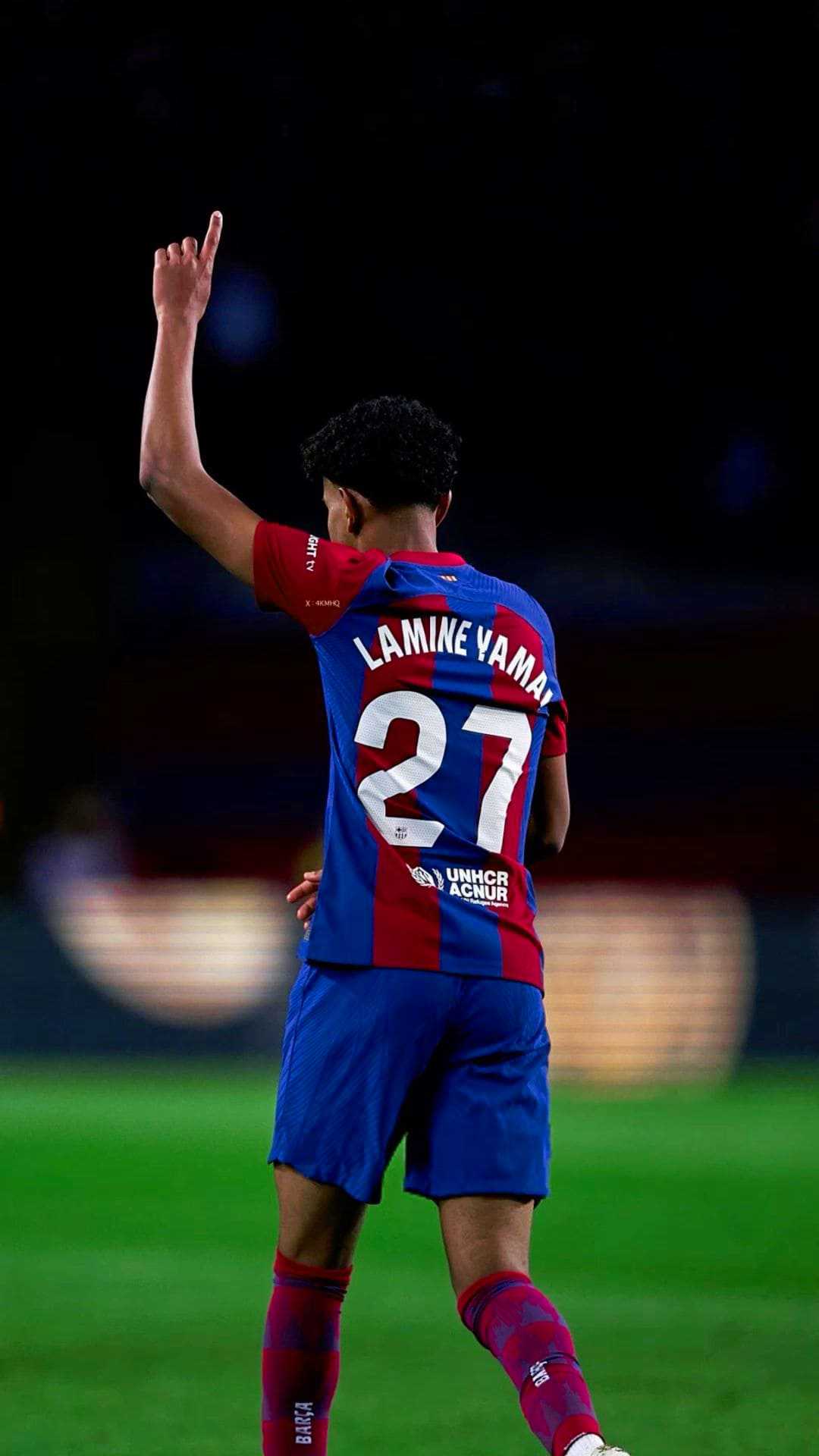 Lamine Yamal of FC Barcelona in action during a match. He is seen from the back, holding up two fingers in celebration, wearing the team's home kit