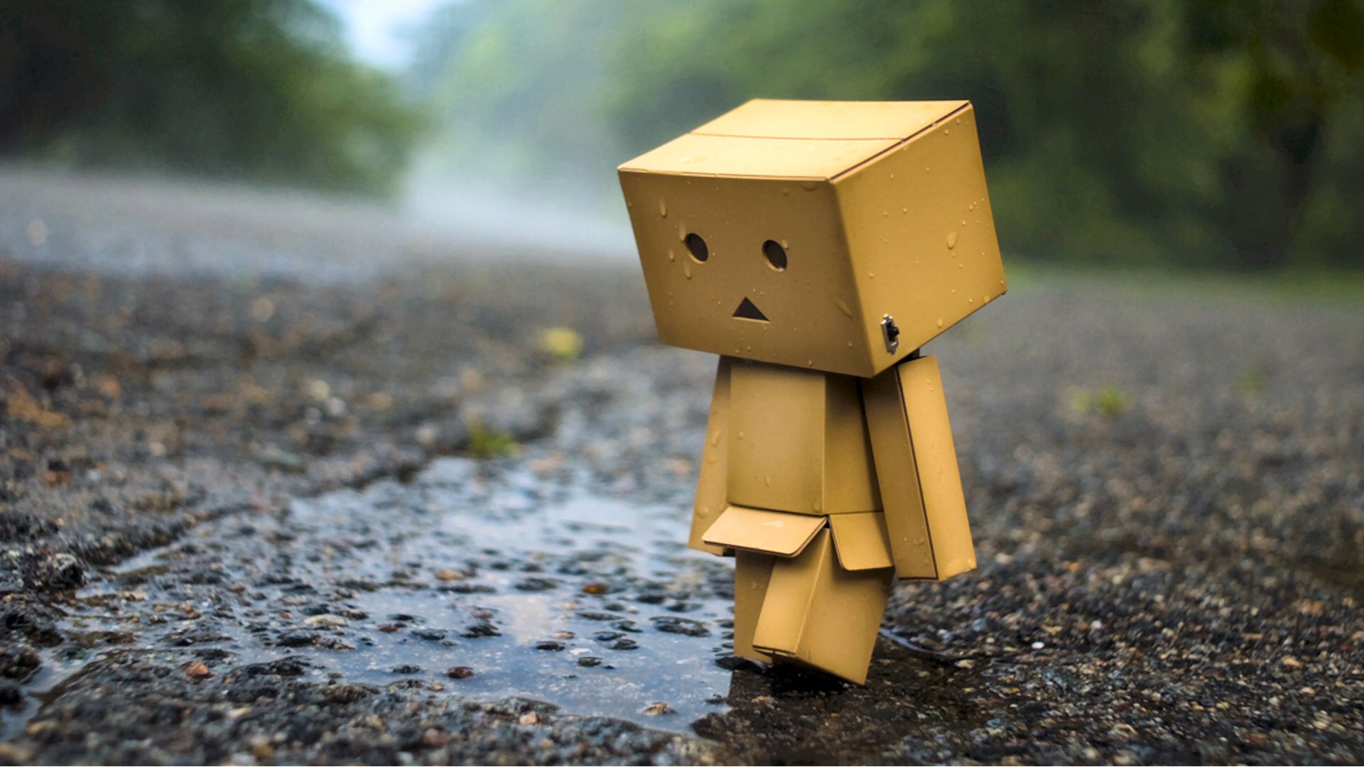 A lonely cardboard figure walks in the rain on a wet asphalt road, evoking feelings of sadness and isolation