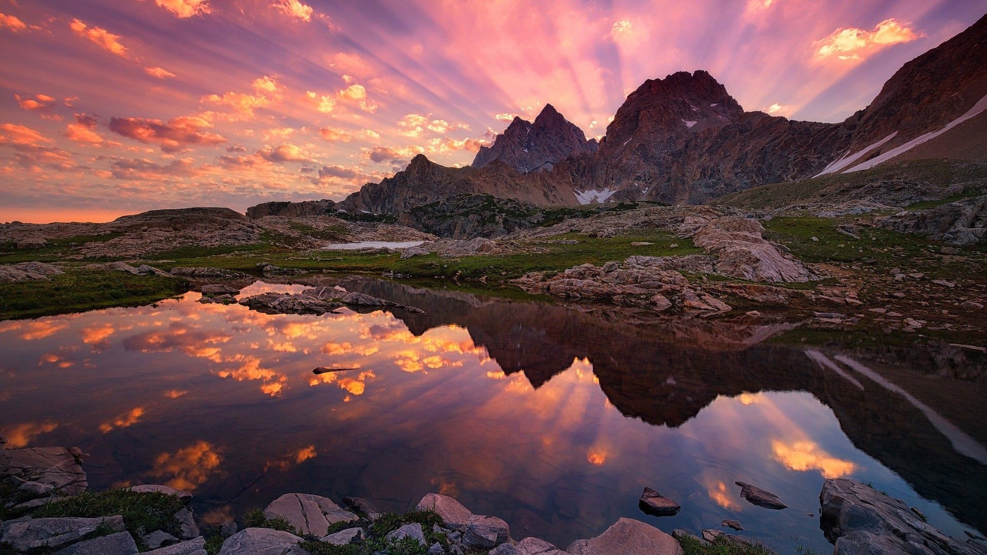 Stunning mountain range reflected in a clear alpine lake at sunset with vibrant pink and orange clouds