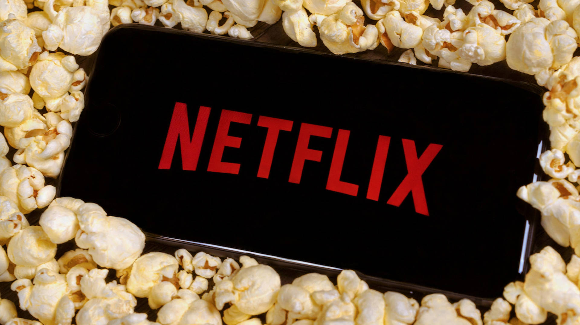 A smartphone displaying the Netflix logo, surrounded by a pile of popcorn, perfect for movie night