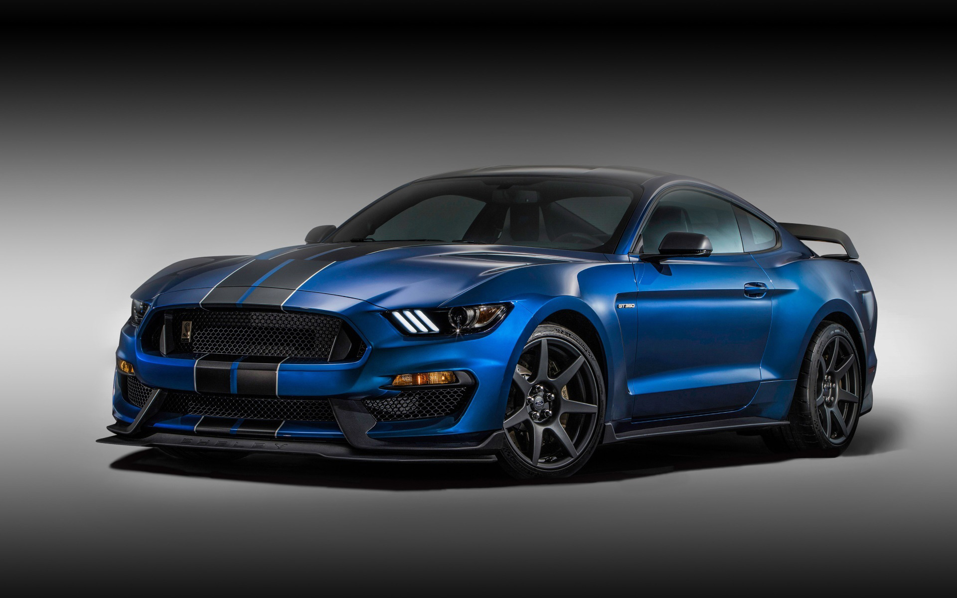 A blue Ford Mustang Shelby GT350 with black racing stripes parked on a gray surface