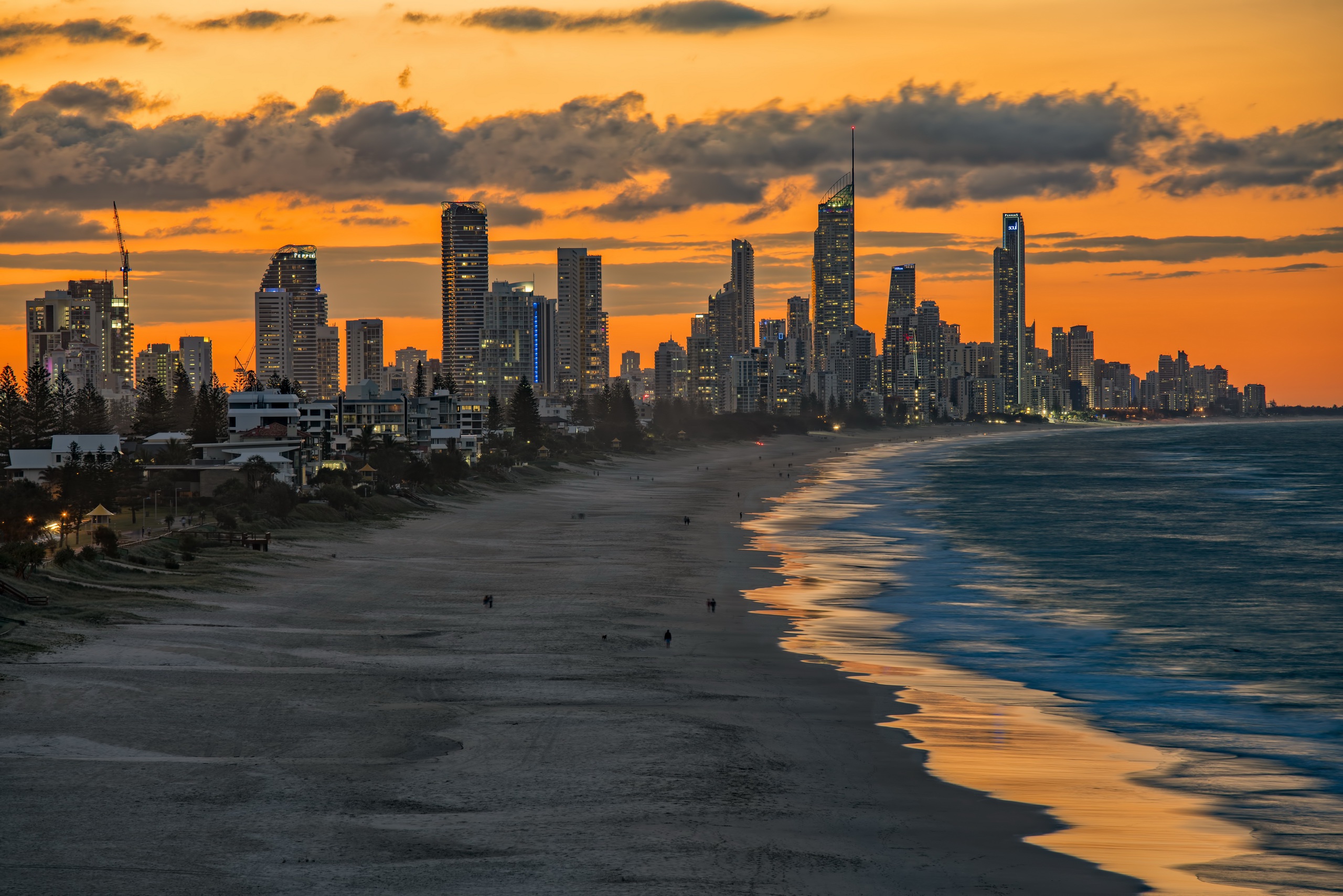 Coastal cityscape at sunset with orange sky and dark sandy beach