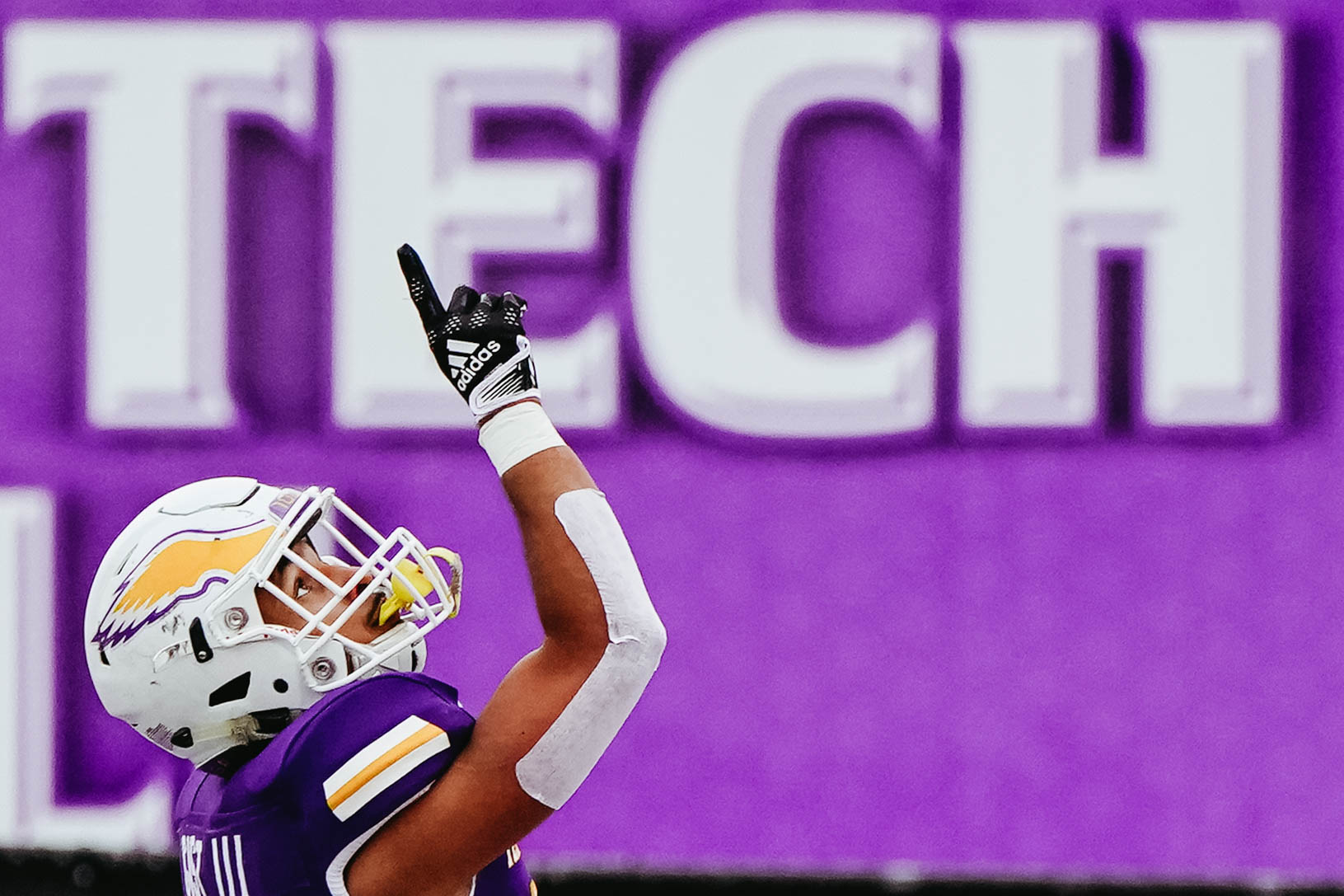 A football player in a purple uniform points towards the sky after making a touchdown during a game