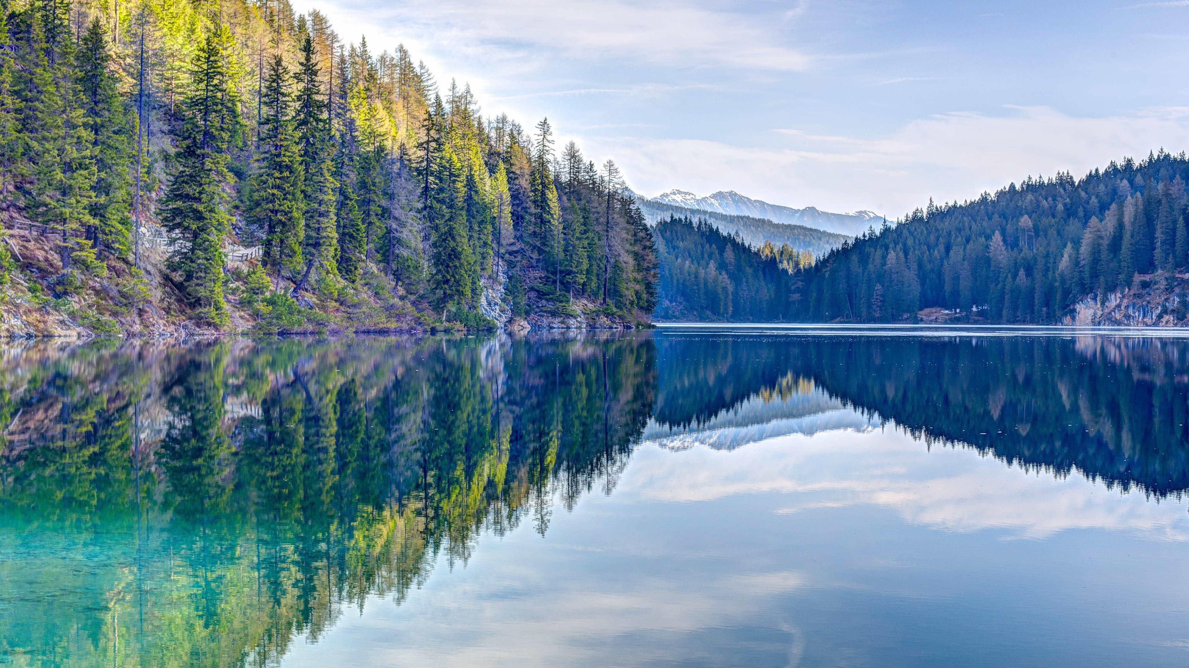 Serene mountain lake reflecting the surrounding forest and snow-capped peaks in 5K HD