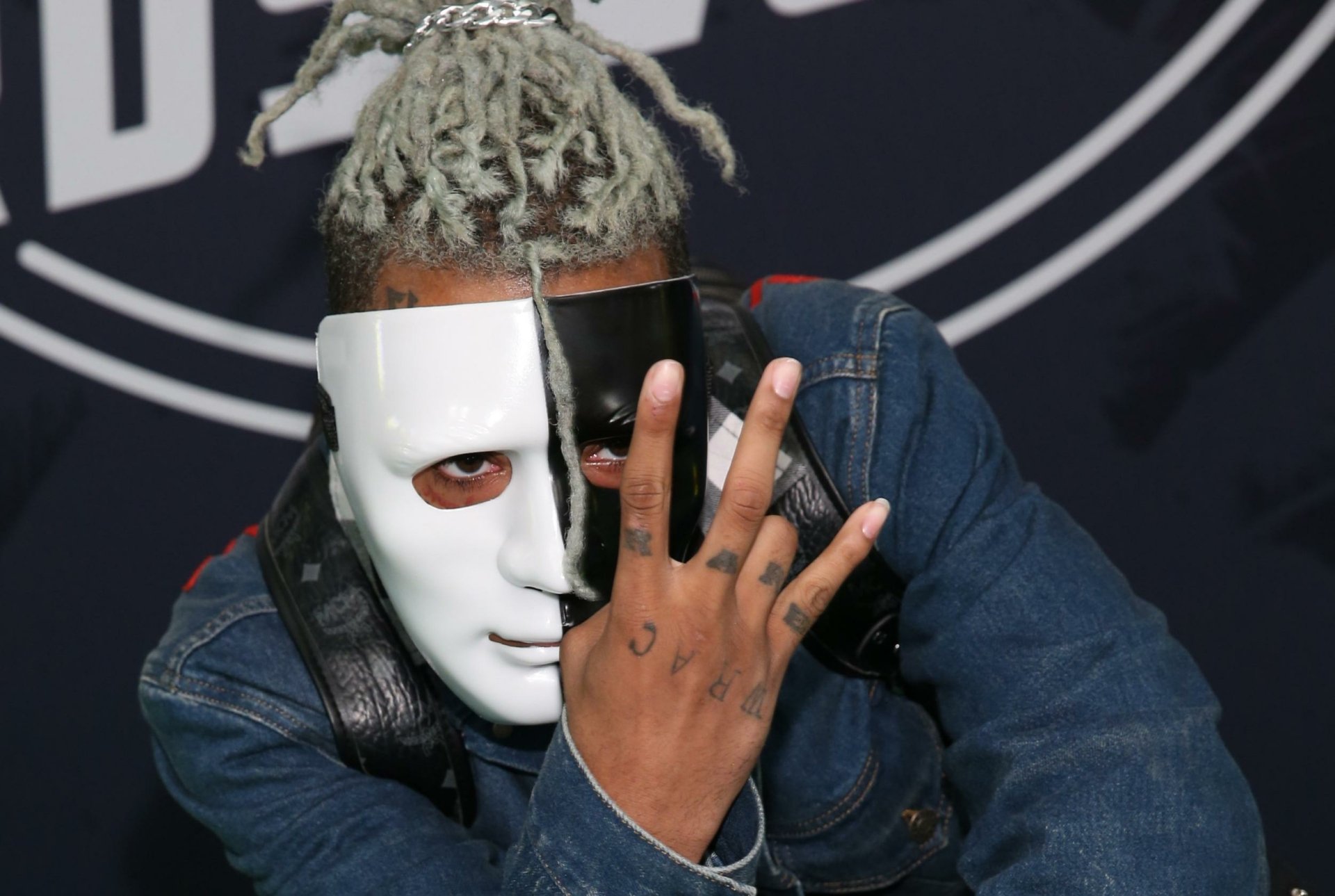 Close-up of XXXTentacion wearing a half-white, half-black mask and making a hand gesture