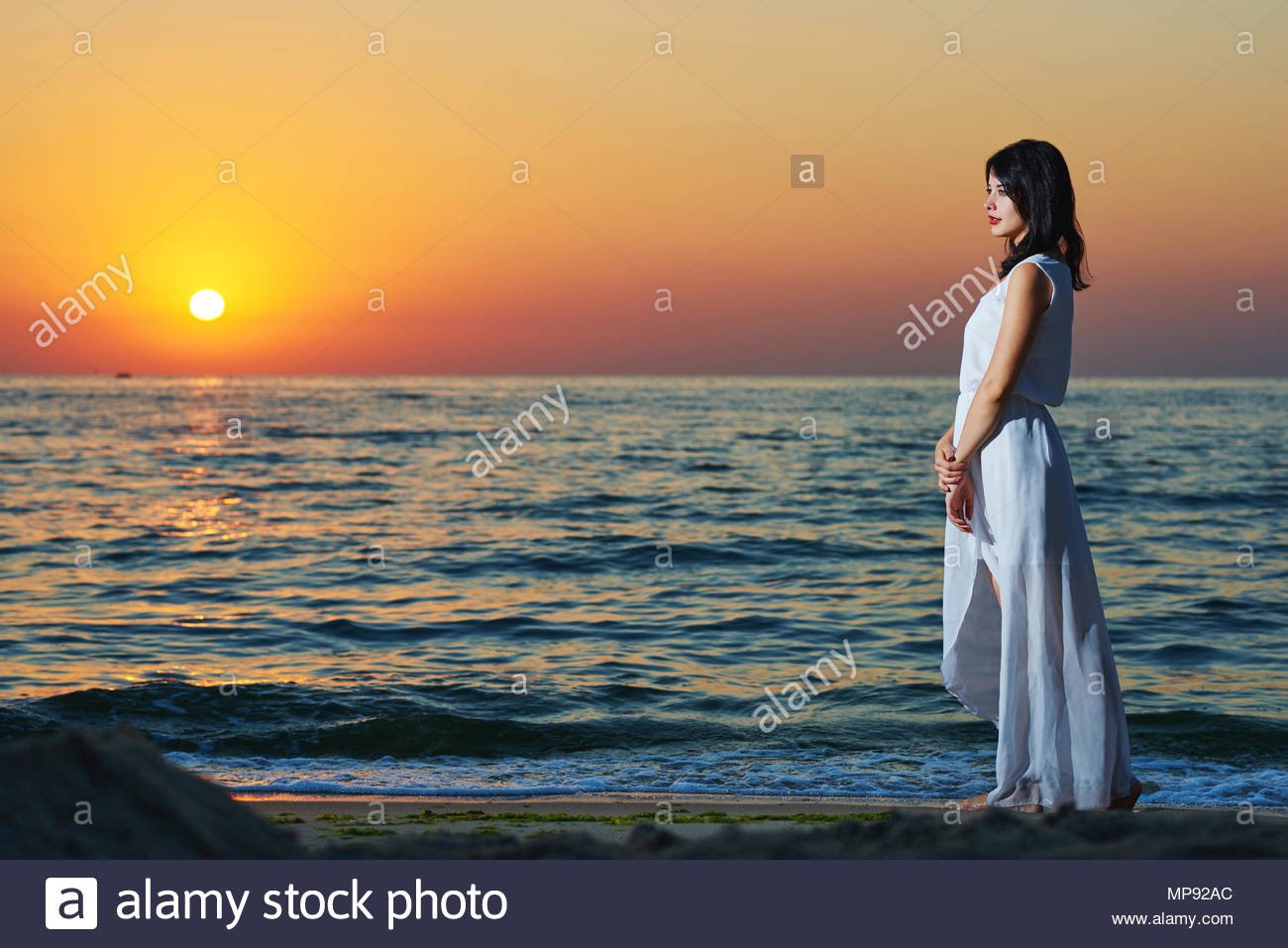Sideview of young woman in white dress standing on sunsets