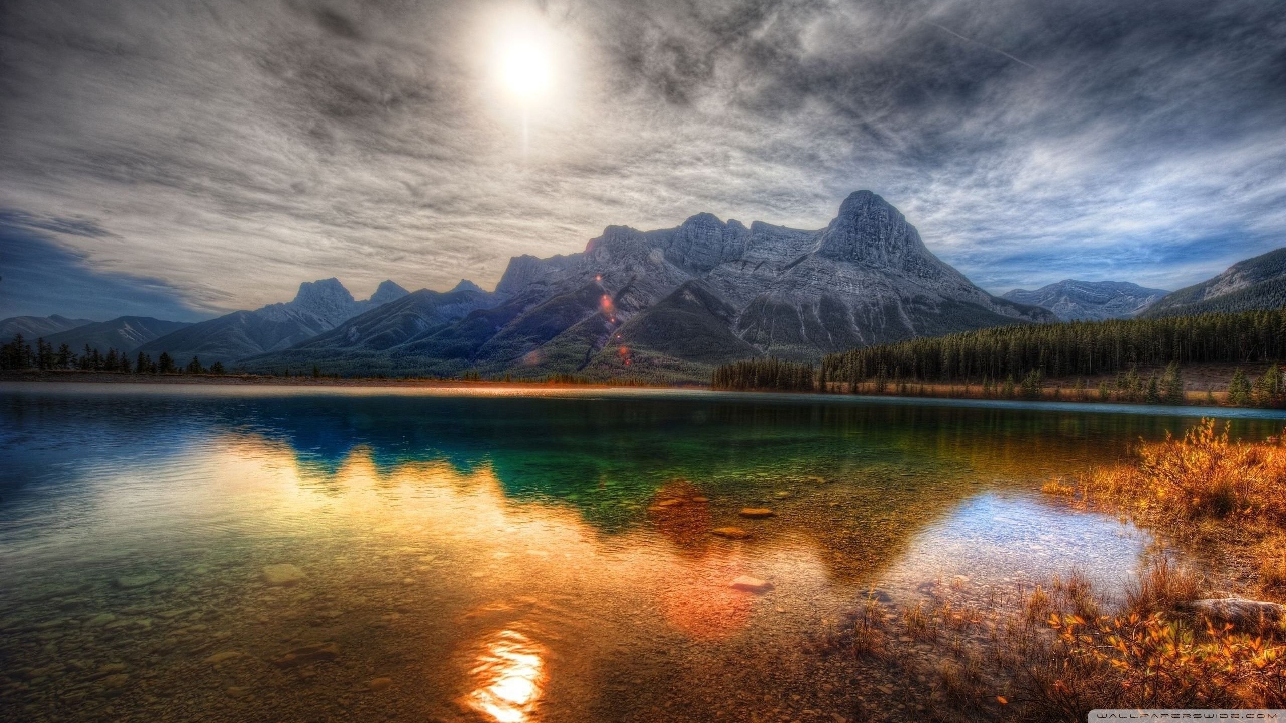 Stunning HDR landscape photograph of a mountain range reflected in a clear lake at sunset