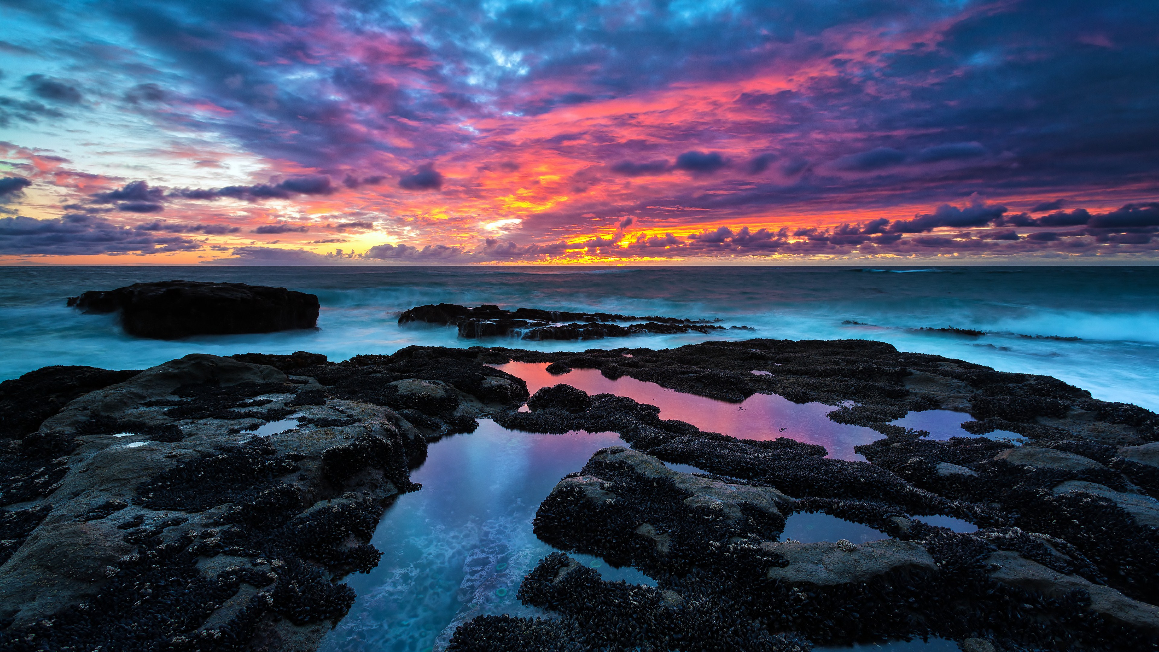 Vivid sunset over a rocky coastline with tide pools reflecting the colorful sky