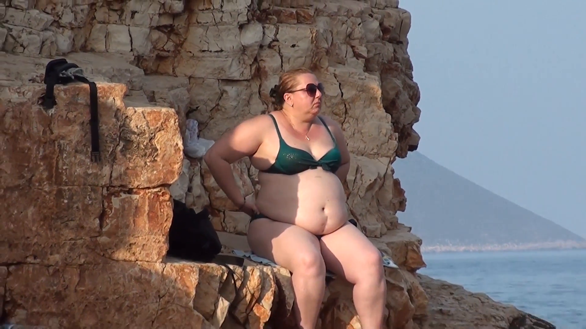 Fat Woman In Bathing Suit Sits On Rock At The Natural Beach Zoom