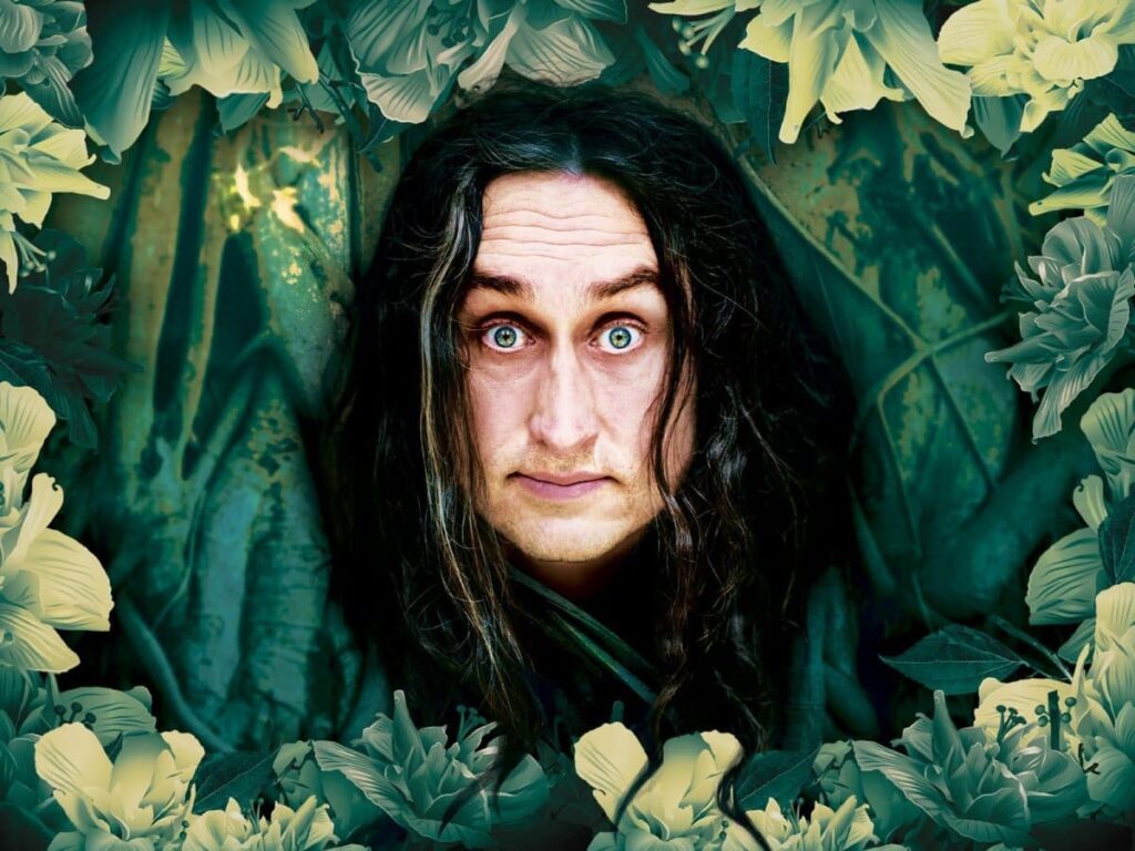 A man with long dark hair, framed by green and yellow floral elements, looks directly at the viewer