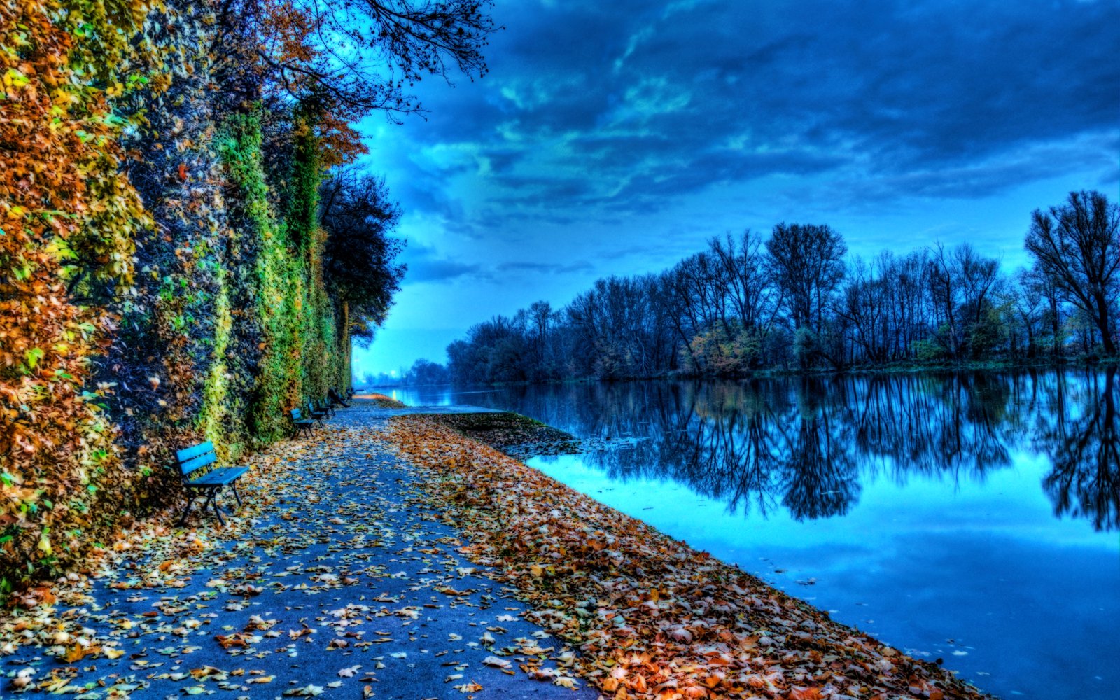 A serene autumn pathway along a river at dusk, with colorful fallen leaves and a vibrant, reflective water surface