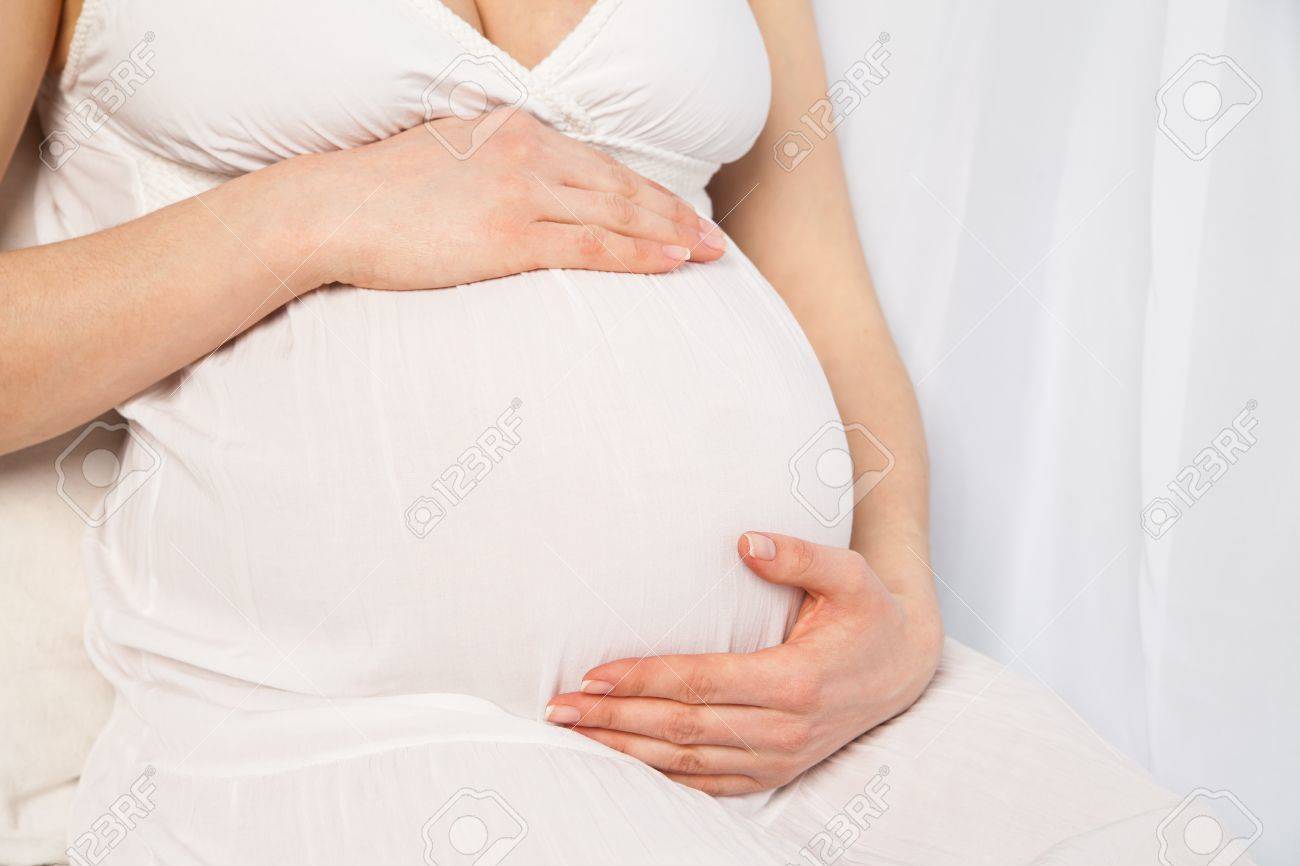 Cute Pregnant Woman In White Dress With Hands On Her Tammy Over