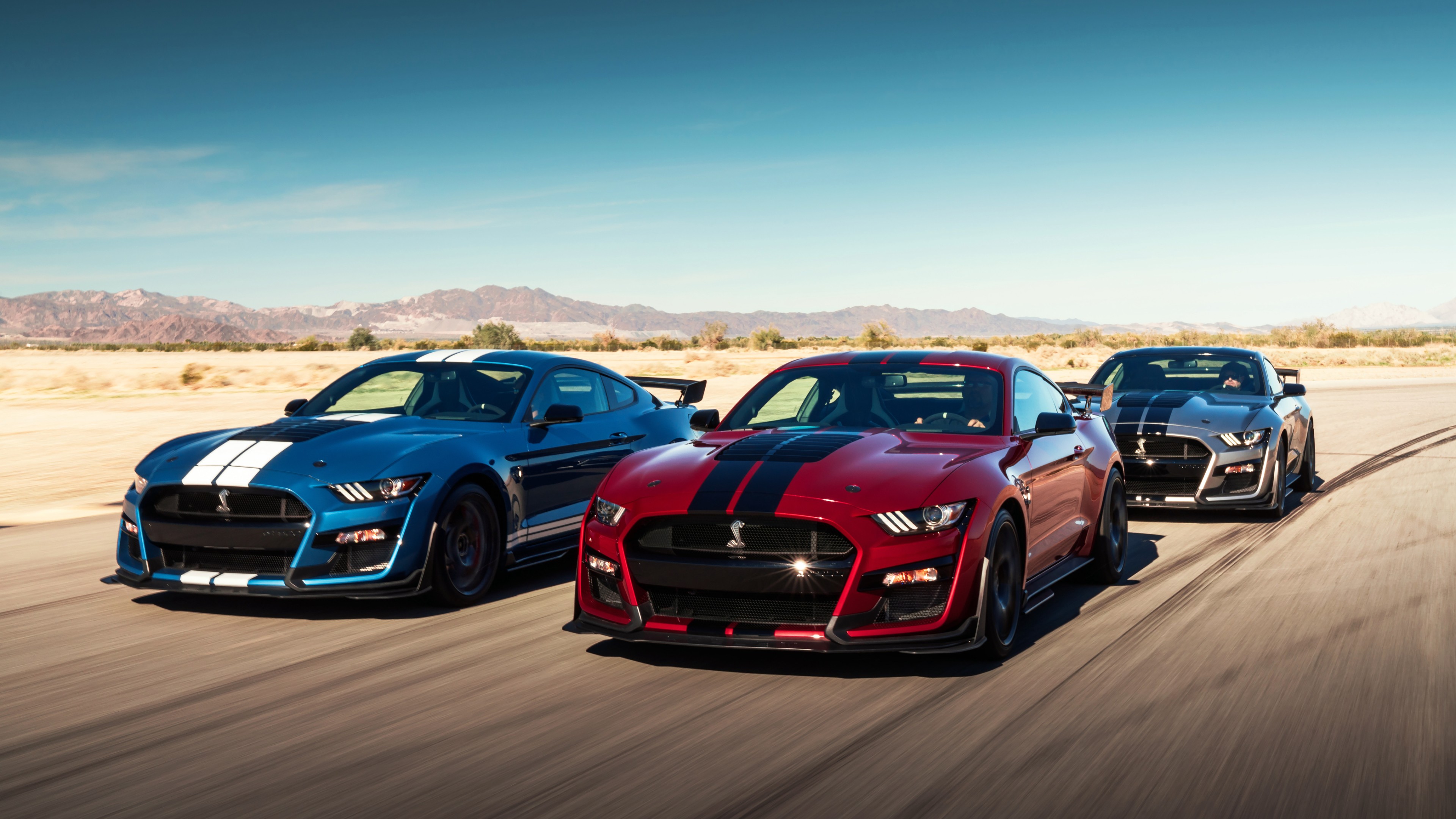 Three Ford Mustang Shelby GT500 cars speeding on a desert track, showcasing power and performance