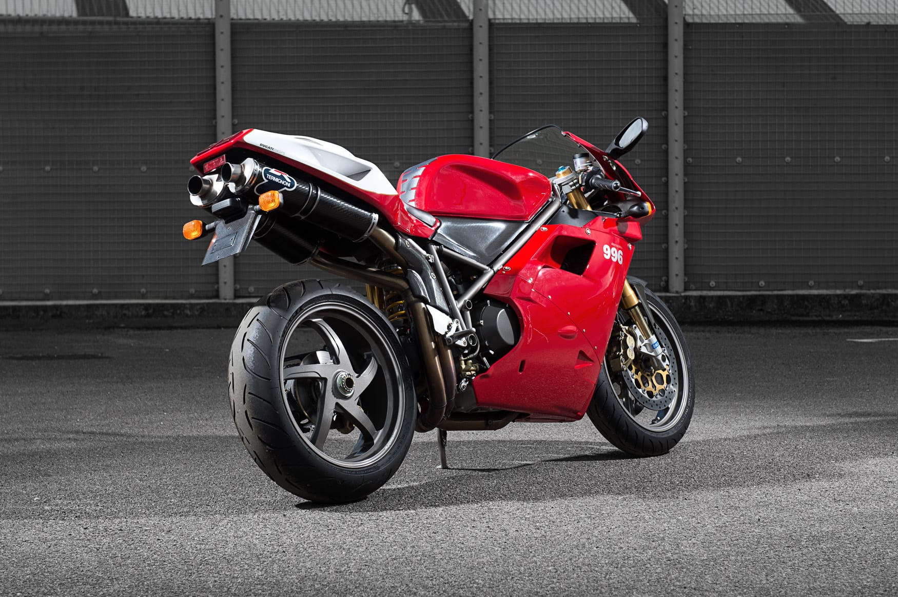 Red and white Ducati 996 parked in front of a metal fence